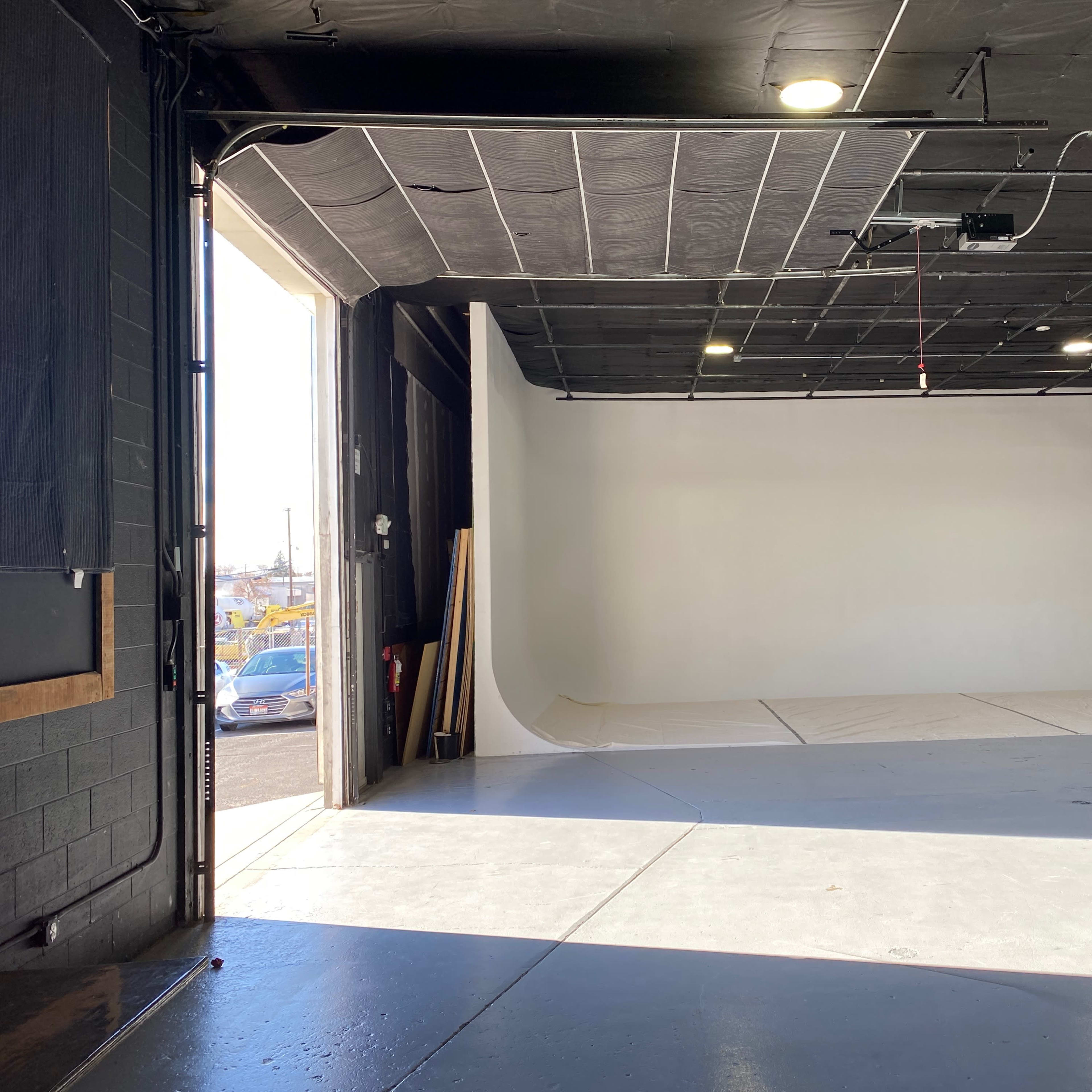 An empty studio space with a large white backdrop and an open garage door allowing natural light to enter.