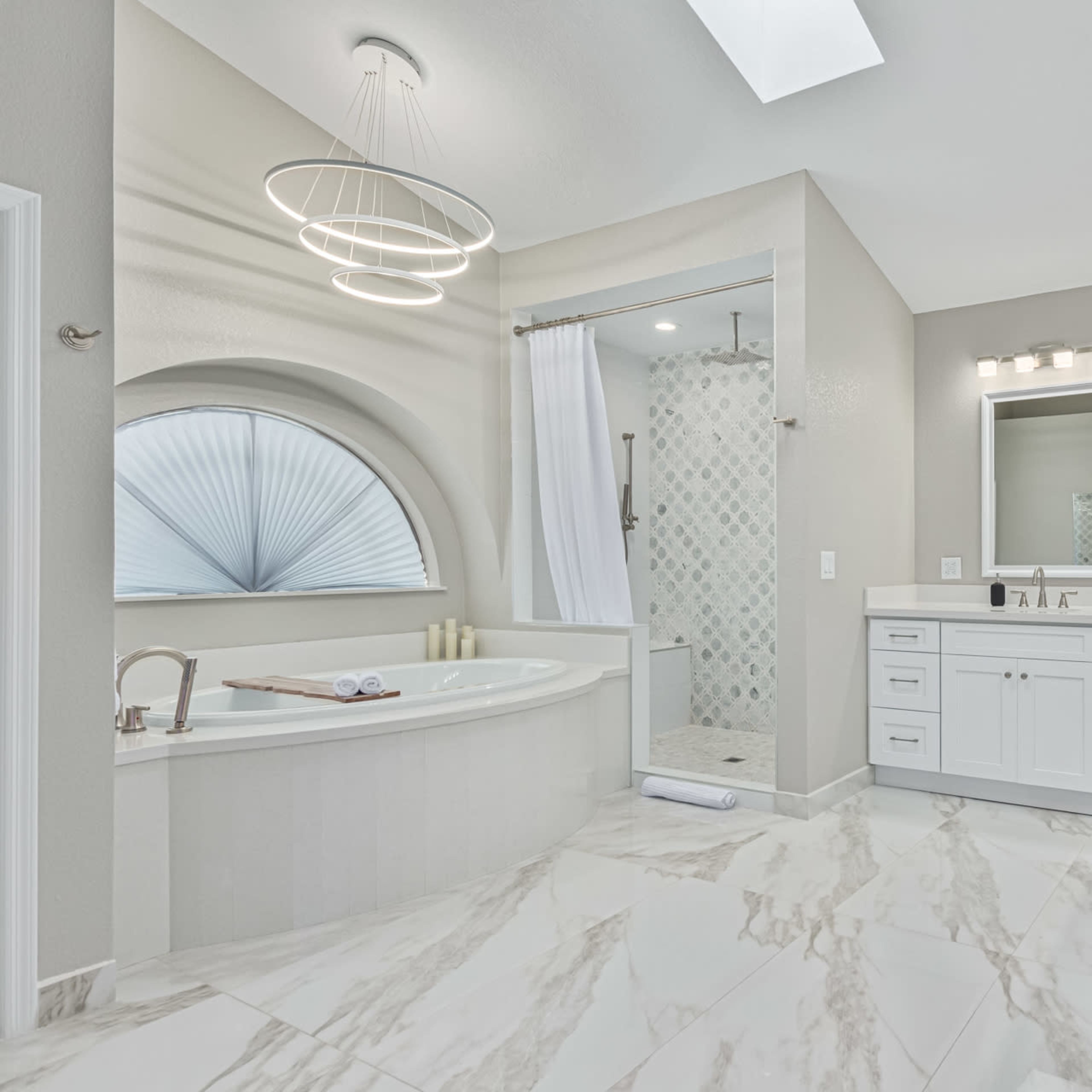 A spacious bathroom with a white freestanding bathtub, a glass shower enclosure, double sinks, and large windows allowing natural light.