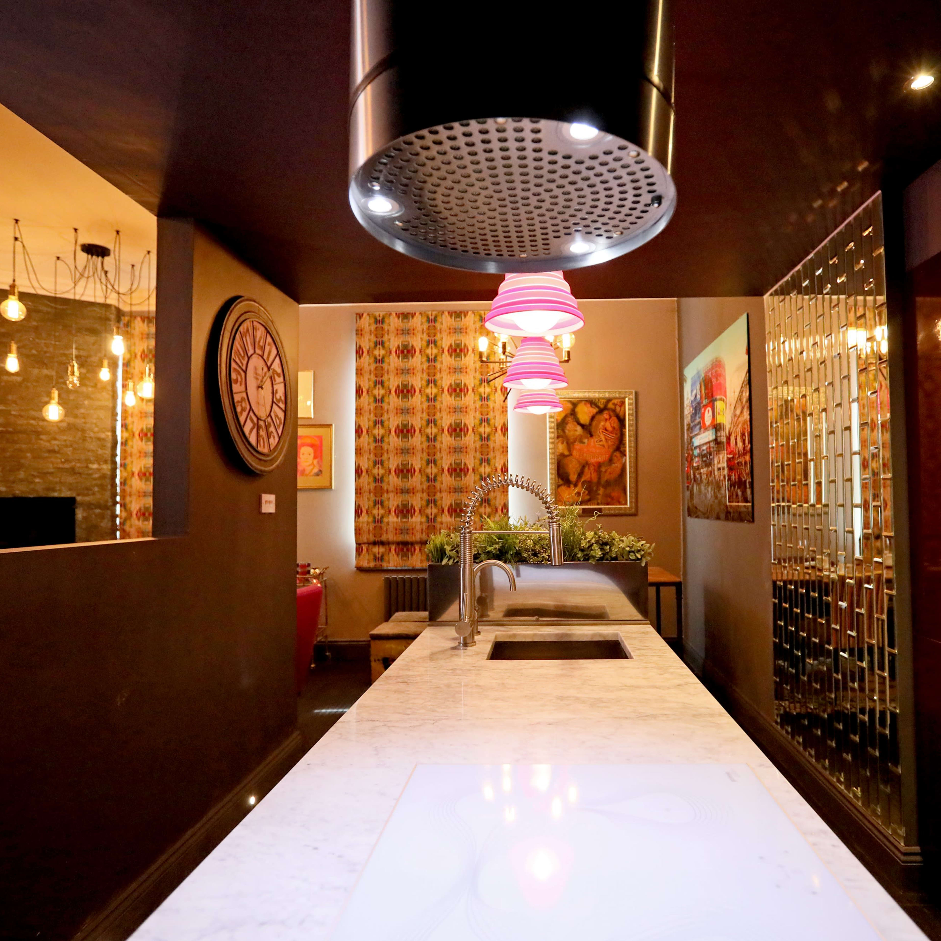 A modern kitchen with a marble island, pendant lighting, and colorful artwork on the walls.
