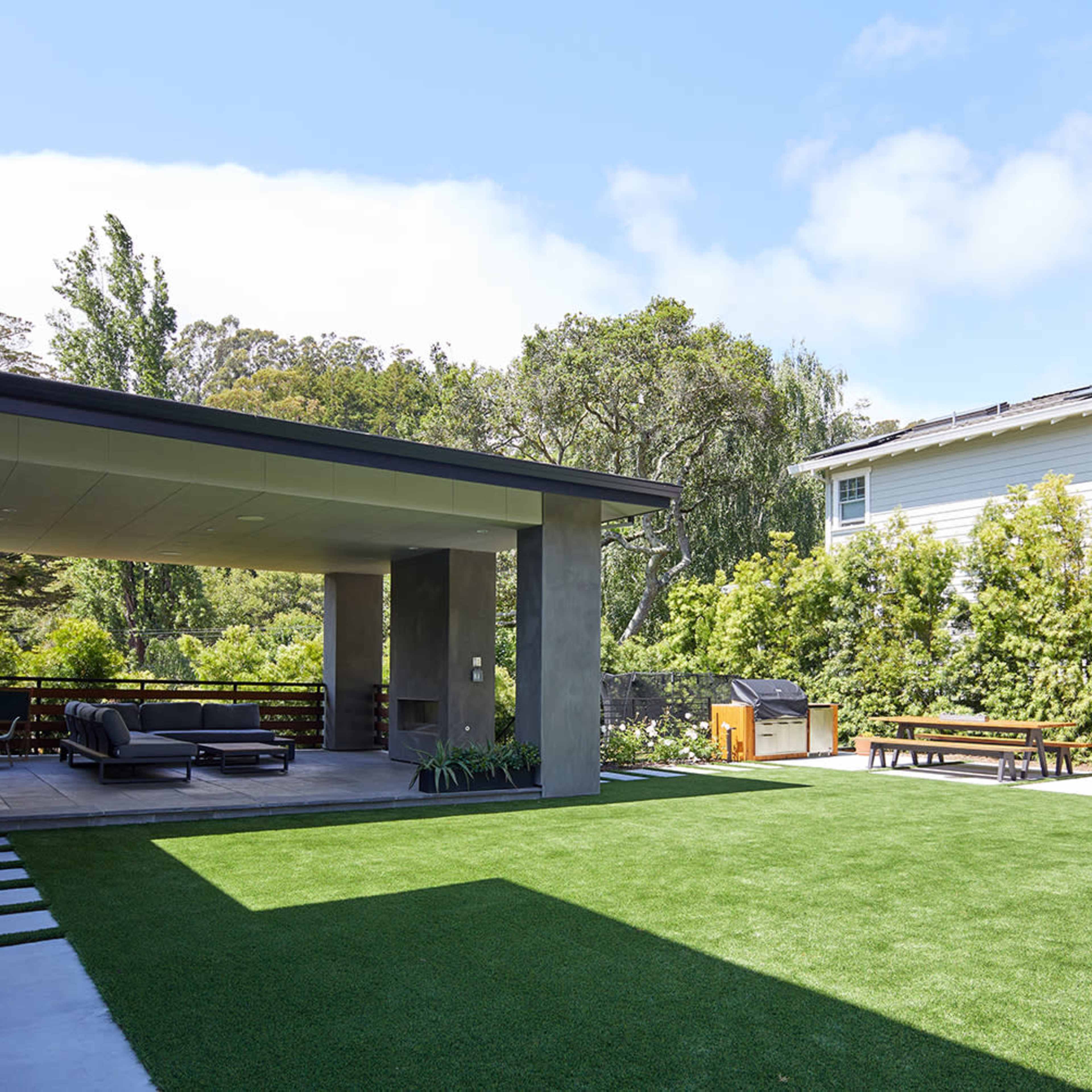 A modern backyard with a green lawn, a covered patio area, outdoor seating, and a picnic table in the background.