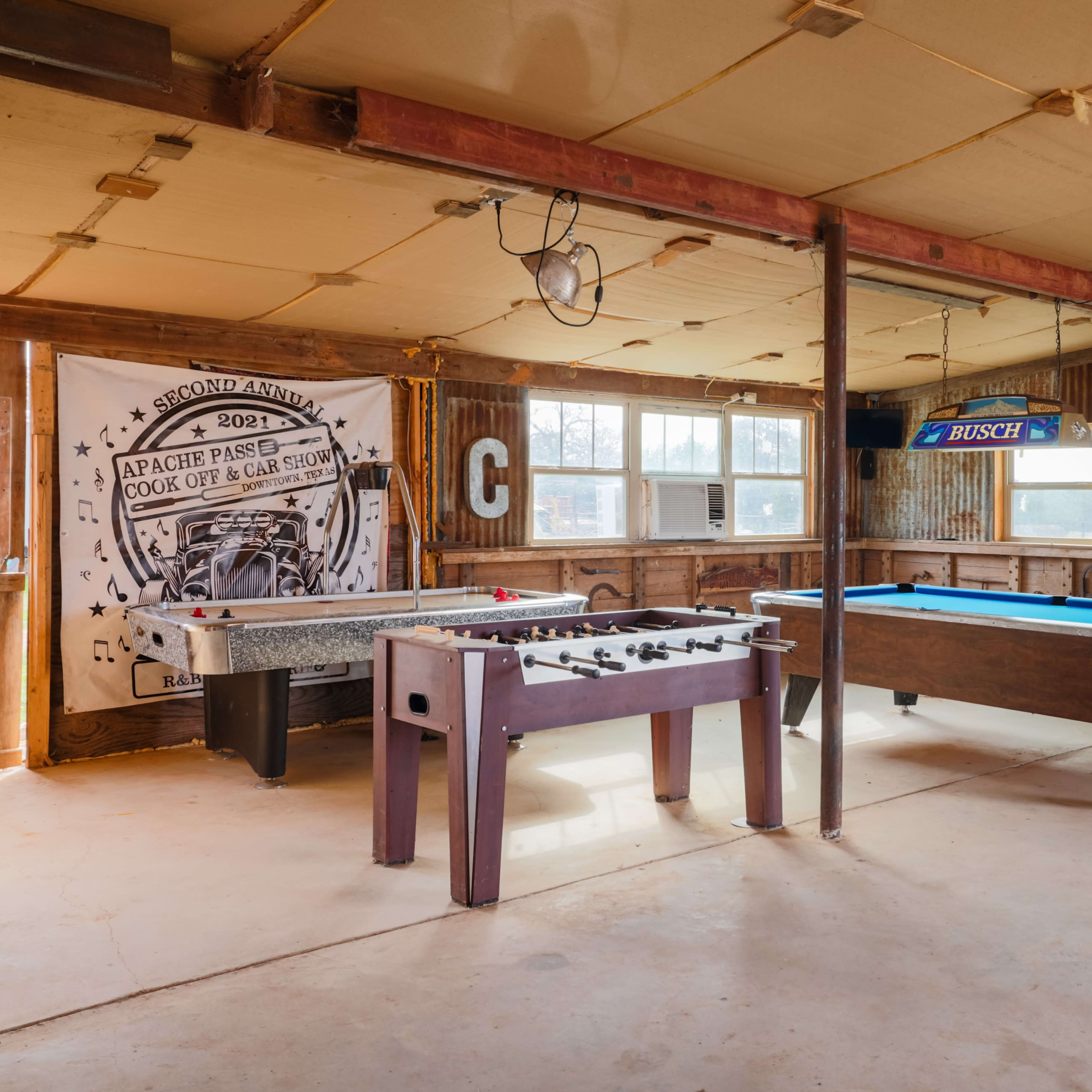 A rustic game room with a foosball table, a pool table, and a large wall banner decorated with a vintage design.