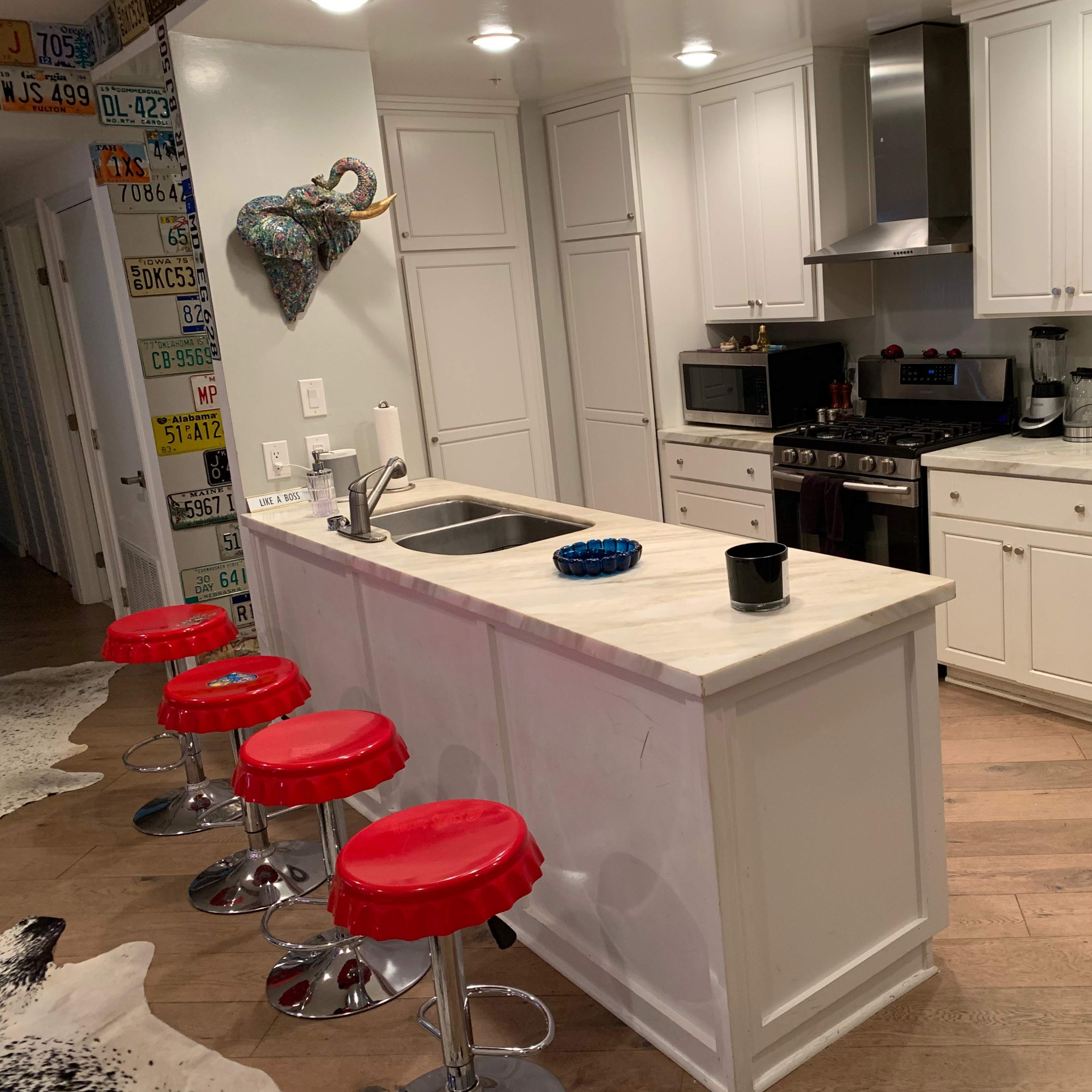 A modern kitchen with white cabinets, a marble countertop island with red stools, and stainless steel appliances.