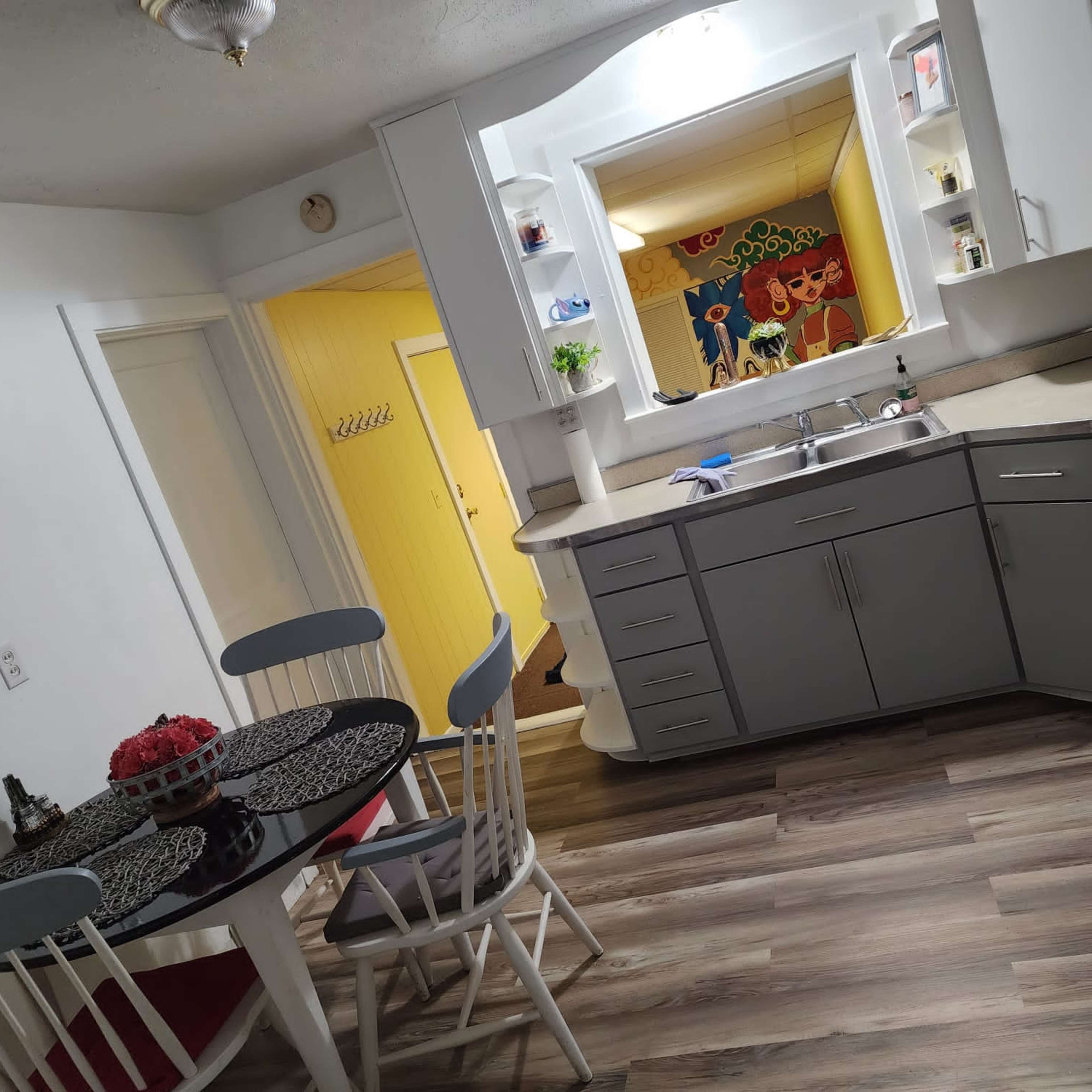 A modern kitchen with gray cabinets, a round dining table, and an open doorway leading to a brightly colored room.