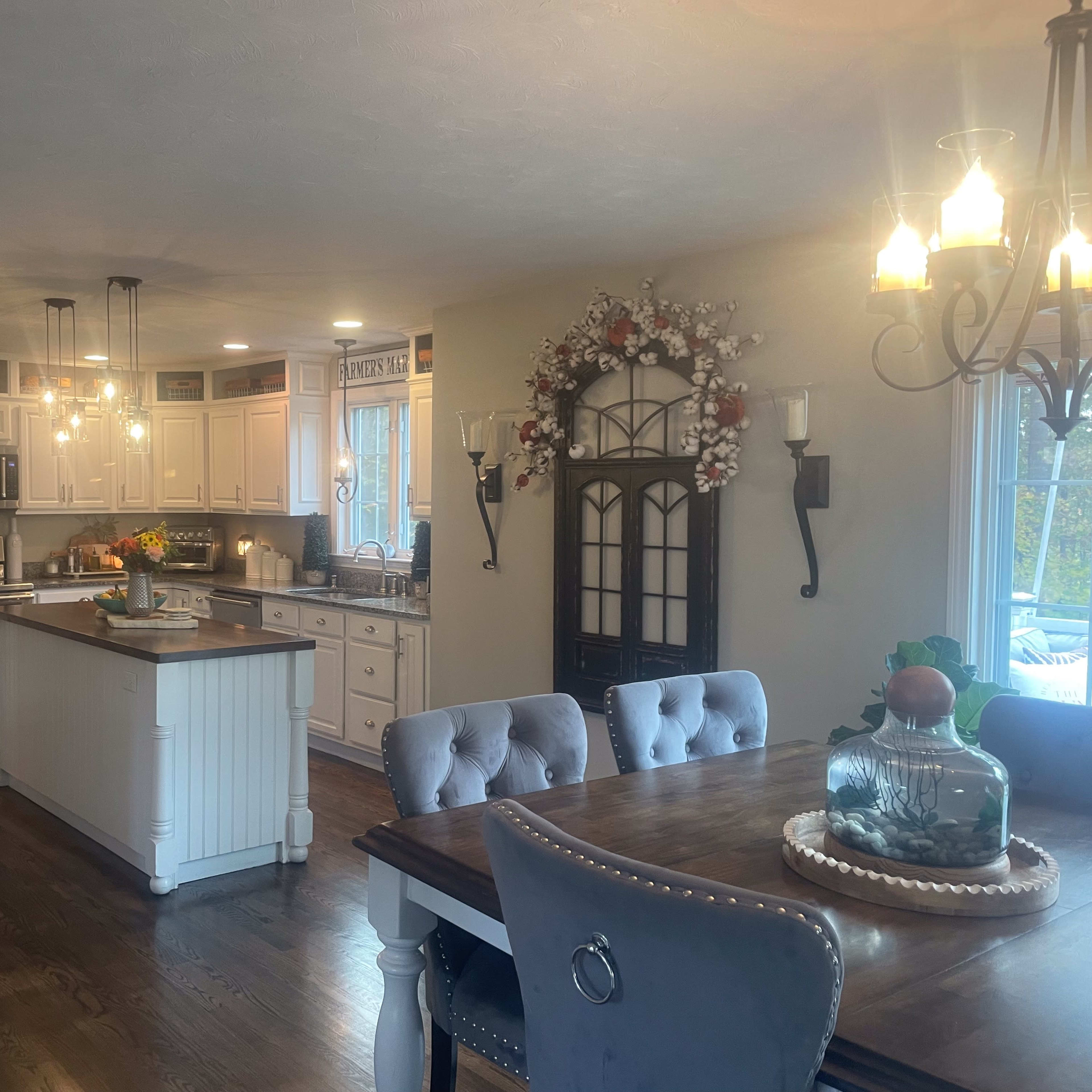 A spacious kitchen with white cabinetry, a central island, and a dining area featuring a wooden table and upholstered chairs.