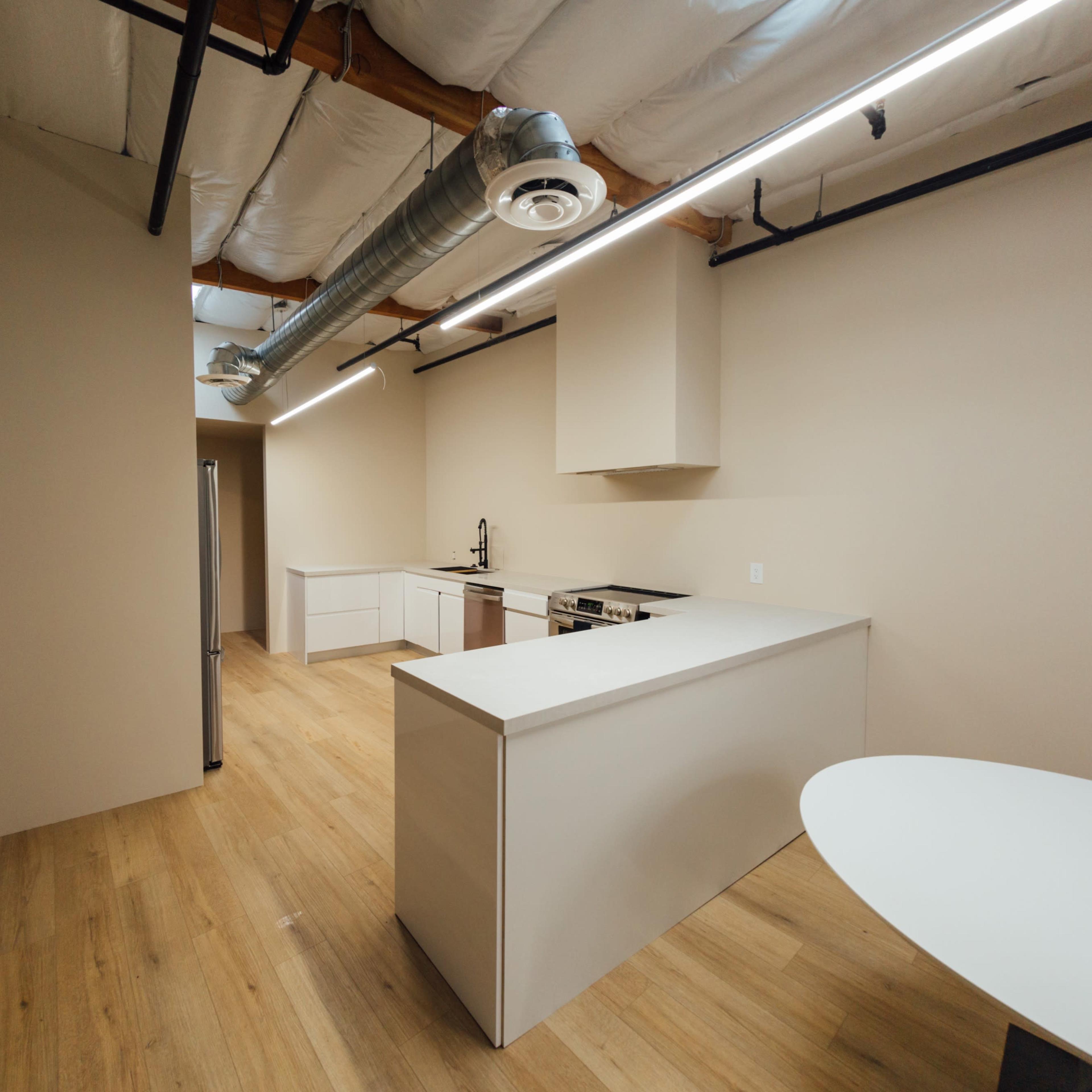 A modern kitchen space with white cabinetry, stainless steel appliances, a large countertop, and wooden flooring.