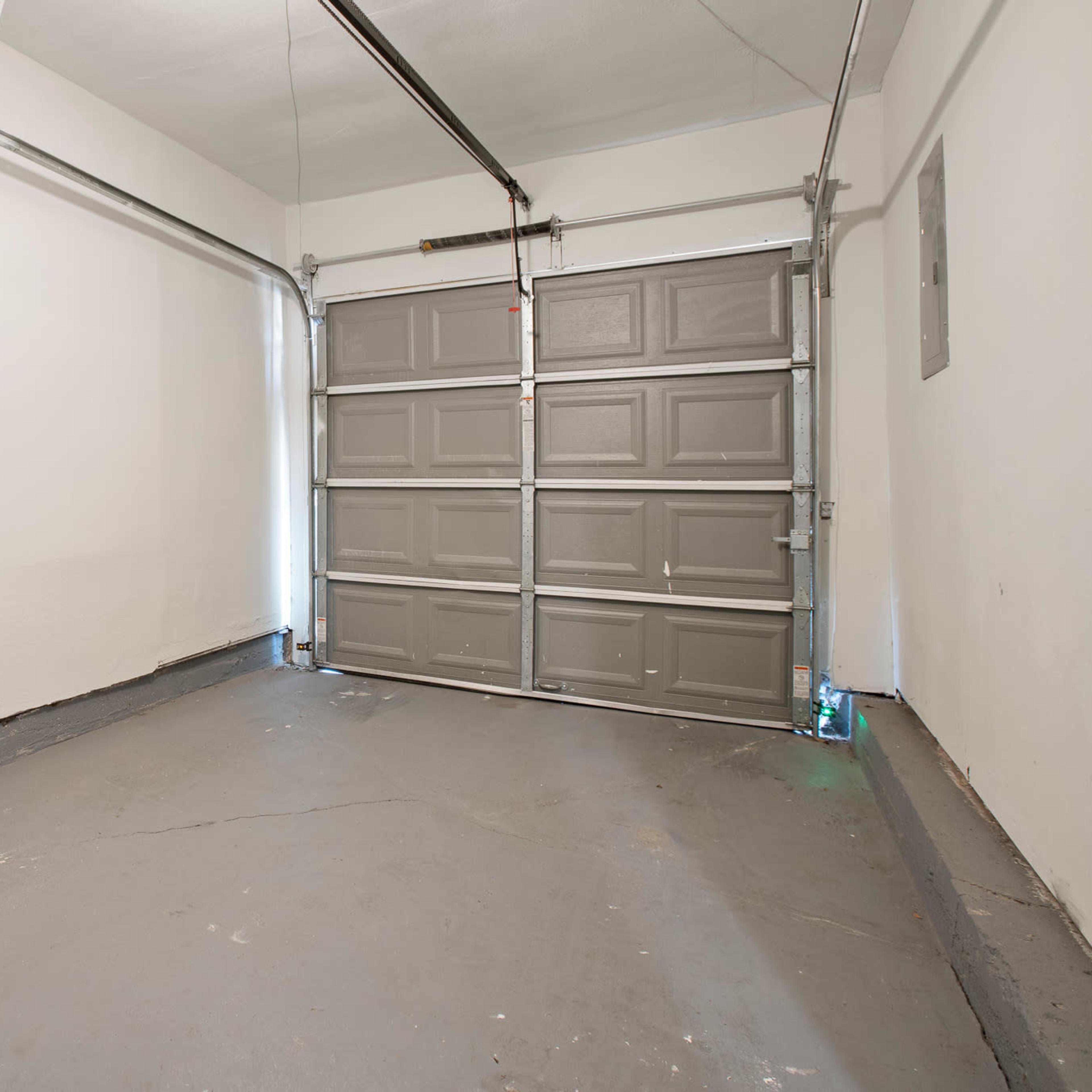 An empty garage with a gray garage door and concrete flooring.