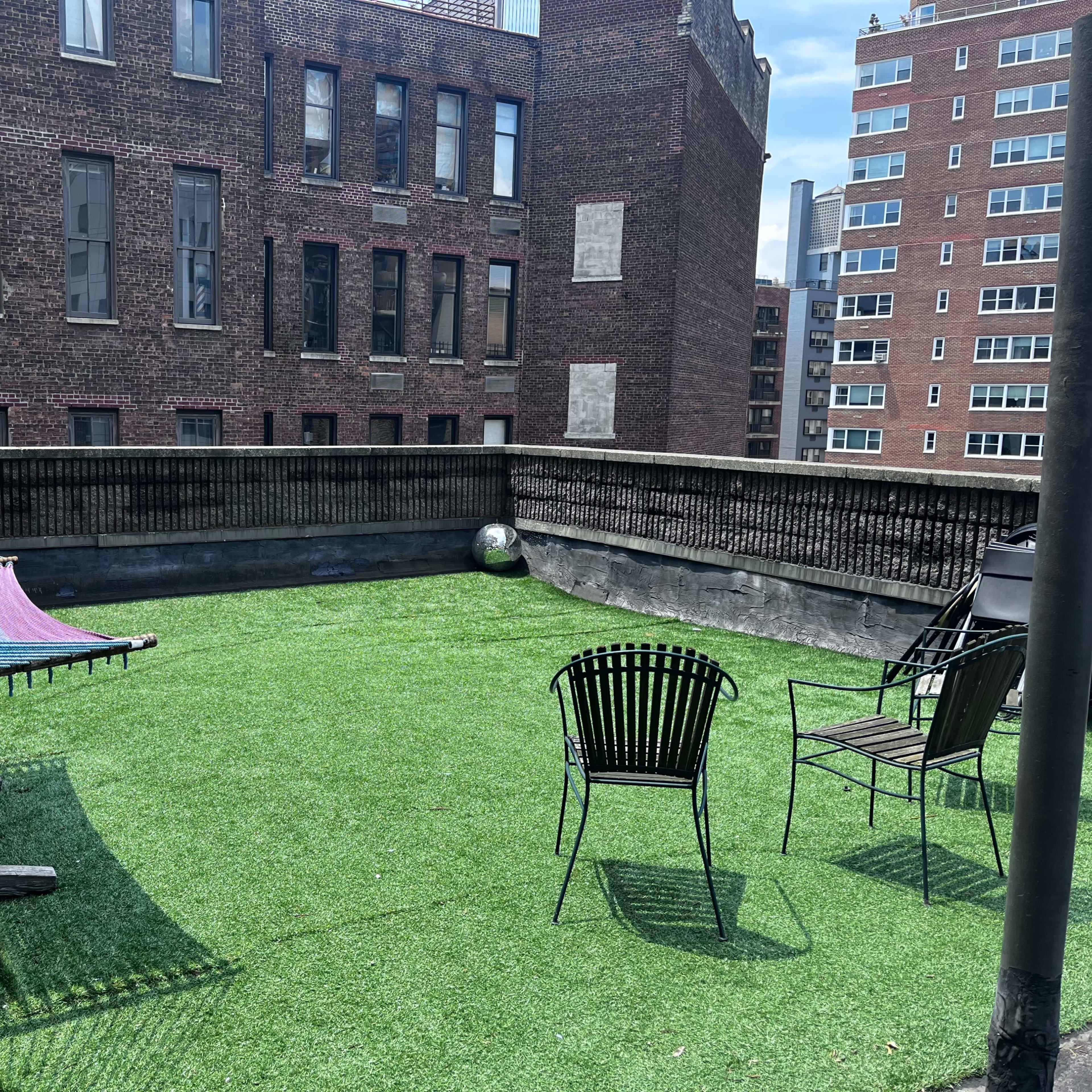 A rooftop terrace with artificial grass, featuring a colorful hammock and two black chairs.