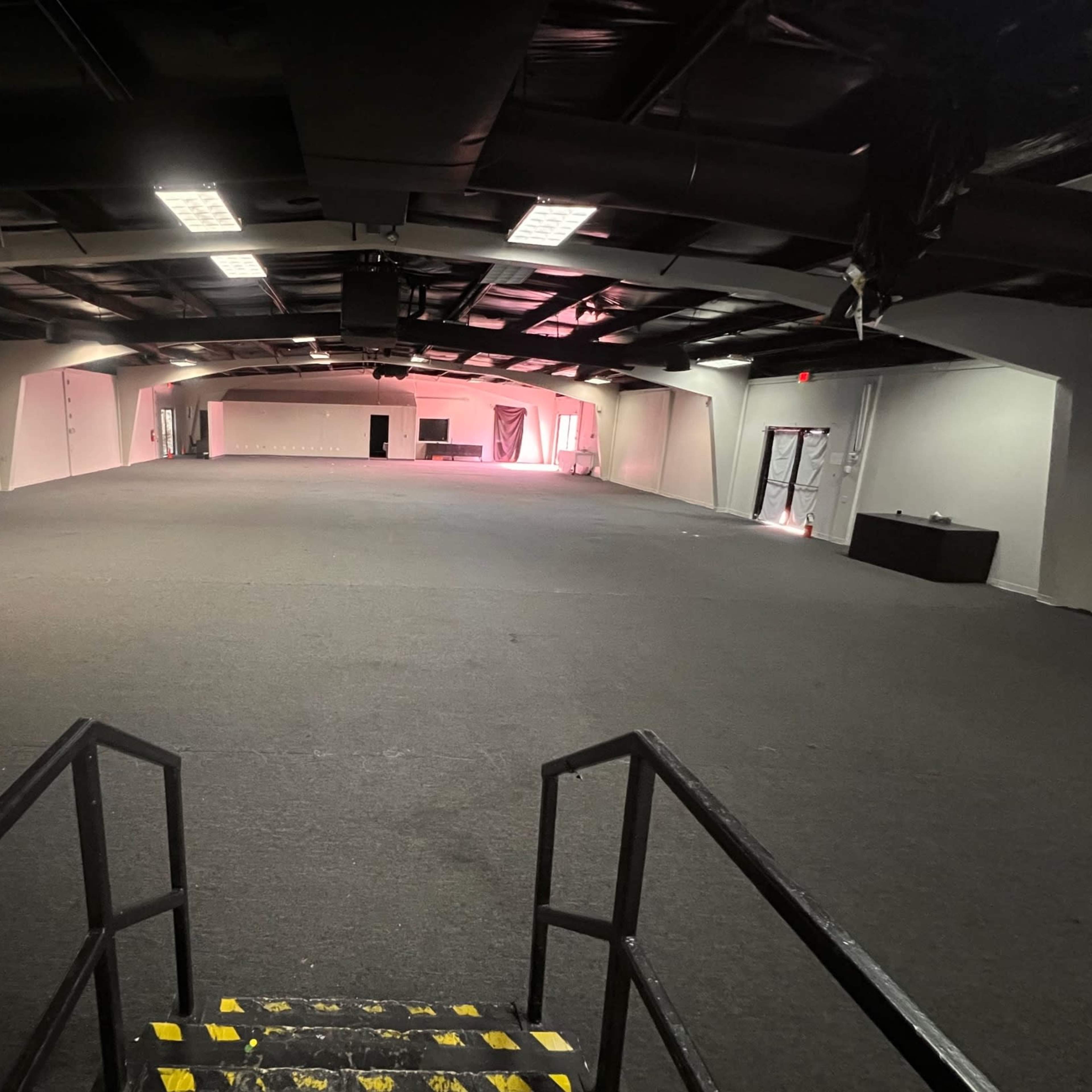 A large, empty interior space with black carpeting, white walls, and overhead lighting.