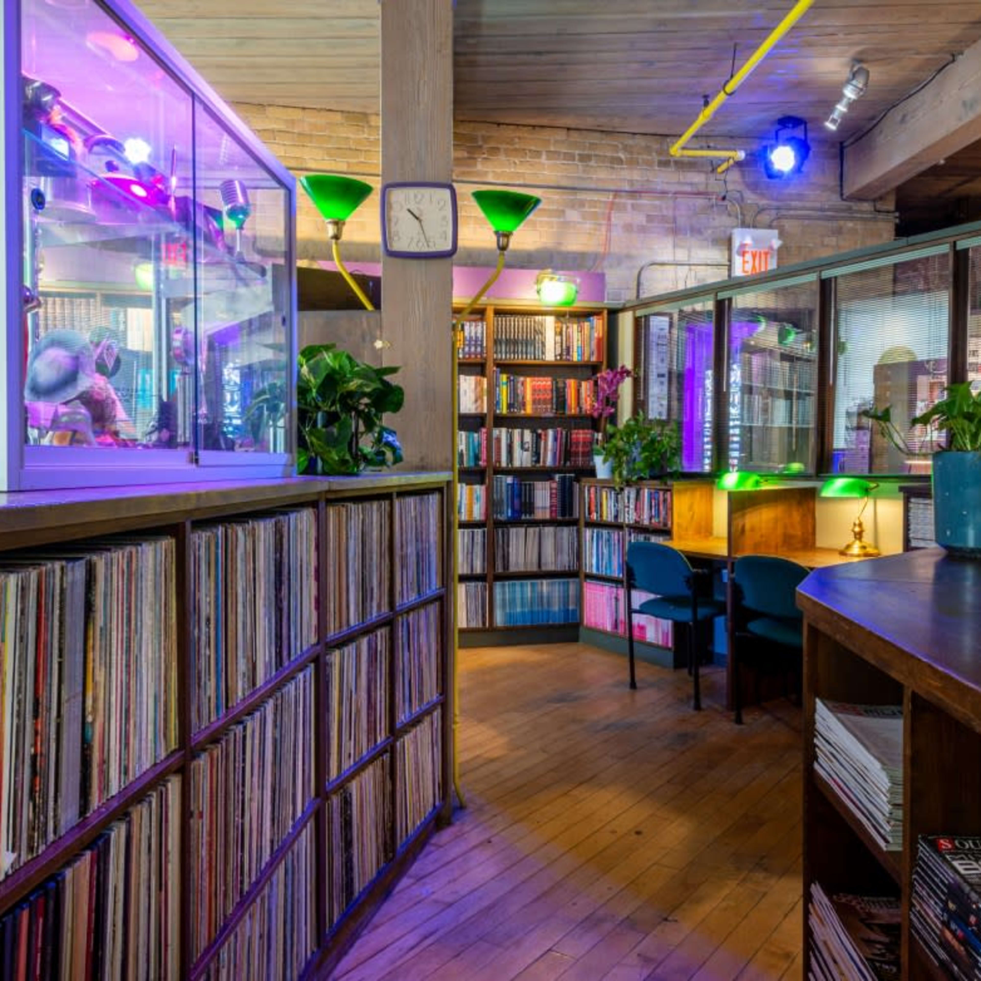 A cozy library space with shelves of books and records, illuminated by colorful lights and featuring a display case.