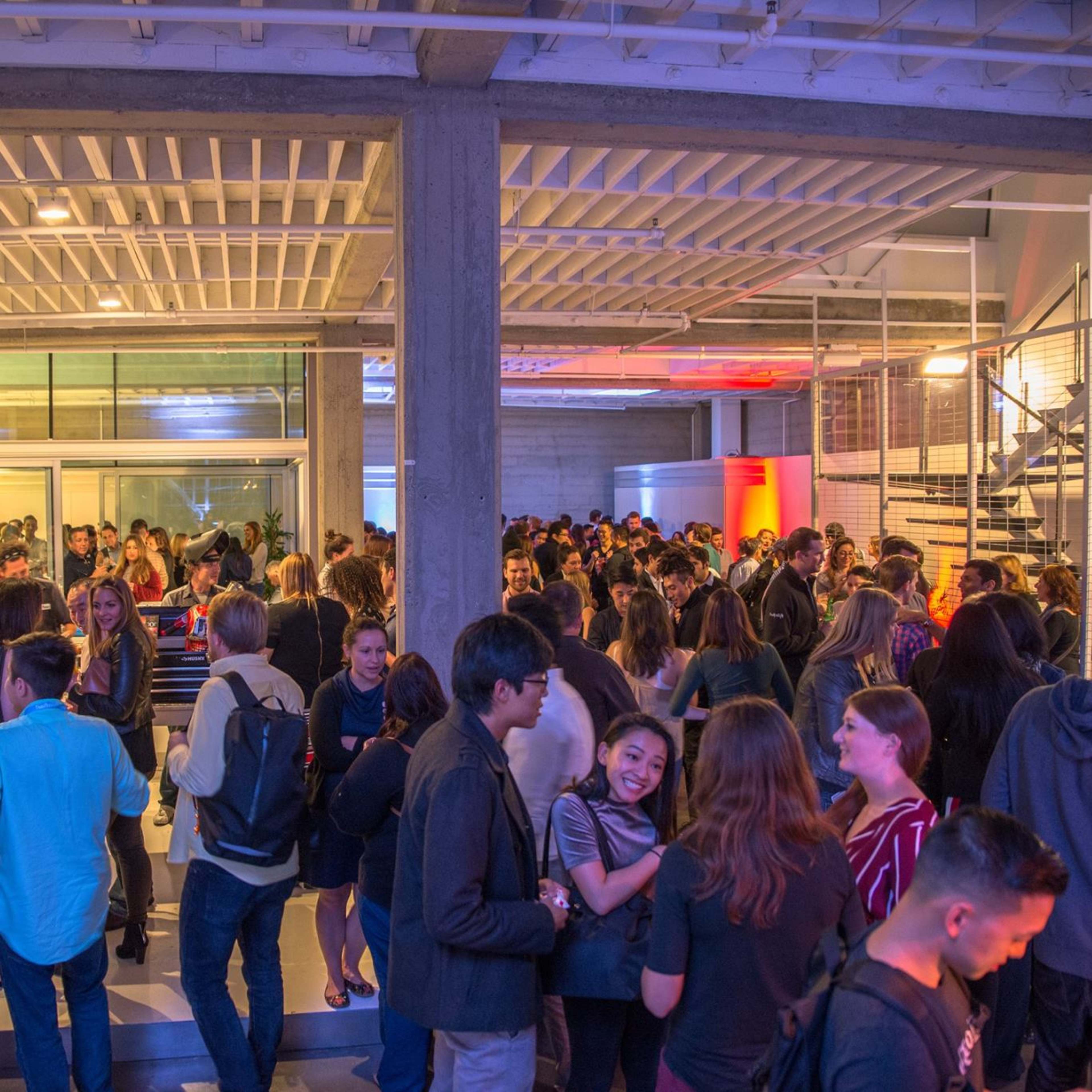 A large group of people socializes at an indoor event featuring modern architecture and bright lighting.