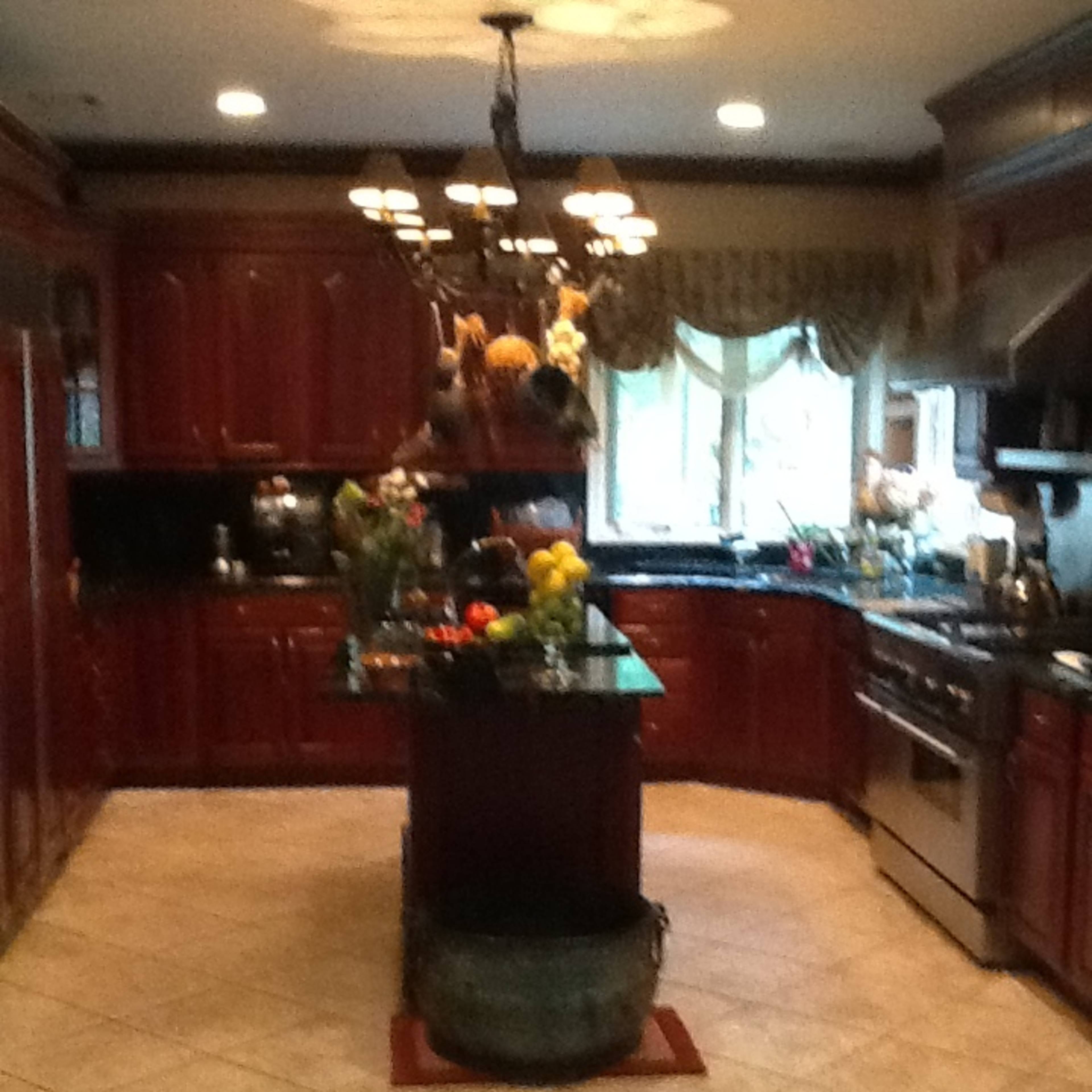 A spacious kitchen features dark wooden cabinets, a central island with fresh fruit, and stainless steel appliances.