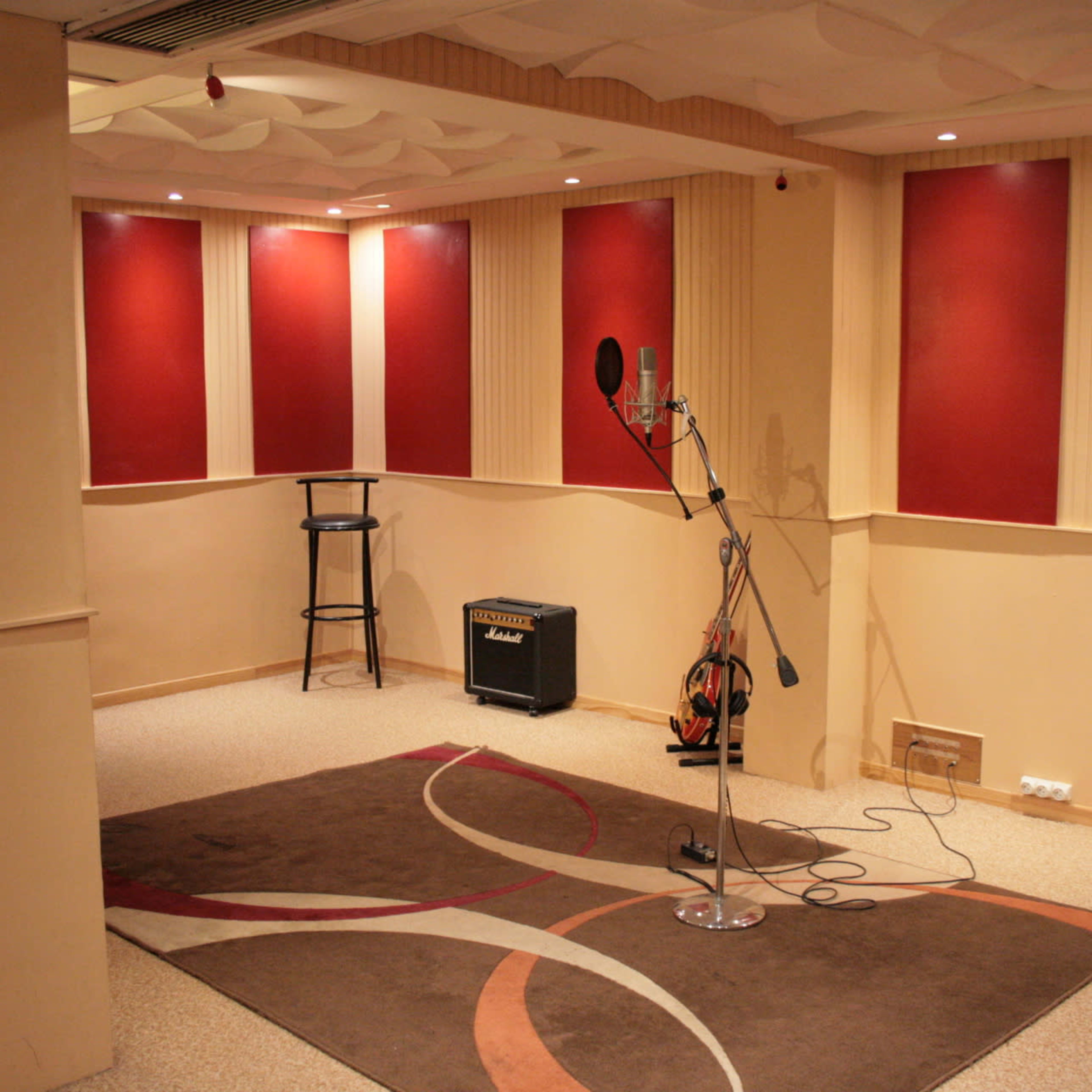 A sound studio with red-accented walls, a microphone on a stand, an amplifier, and a carpeted area.