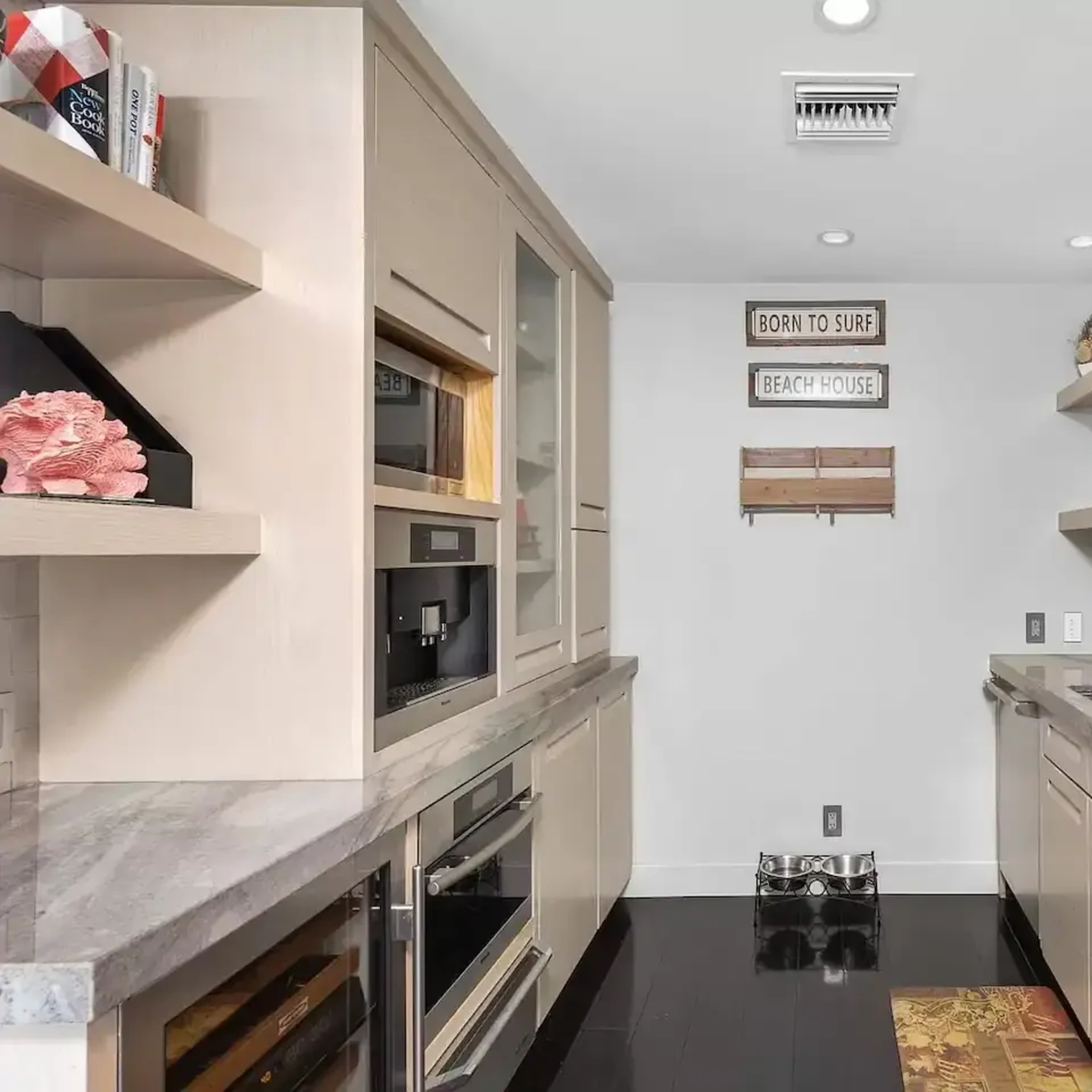 A modern kitchen features stainless steel appliances, light wood cabinetry, and a gray countertop, with decorative signs mounted on the wall.