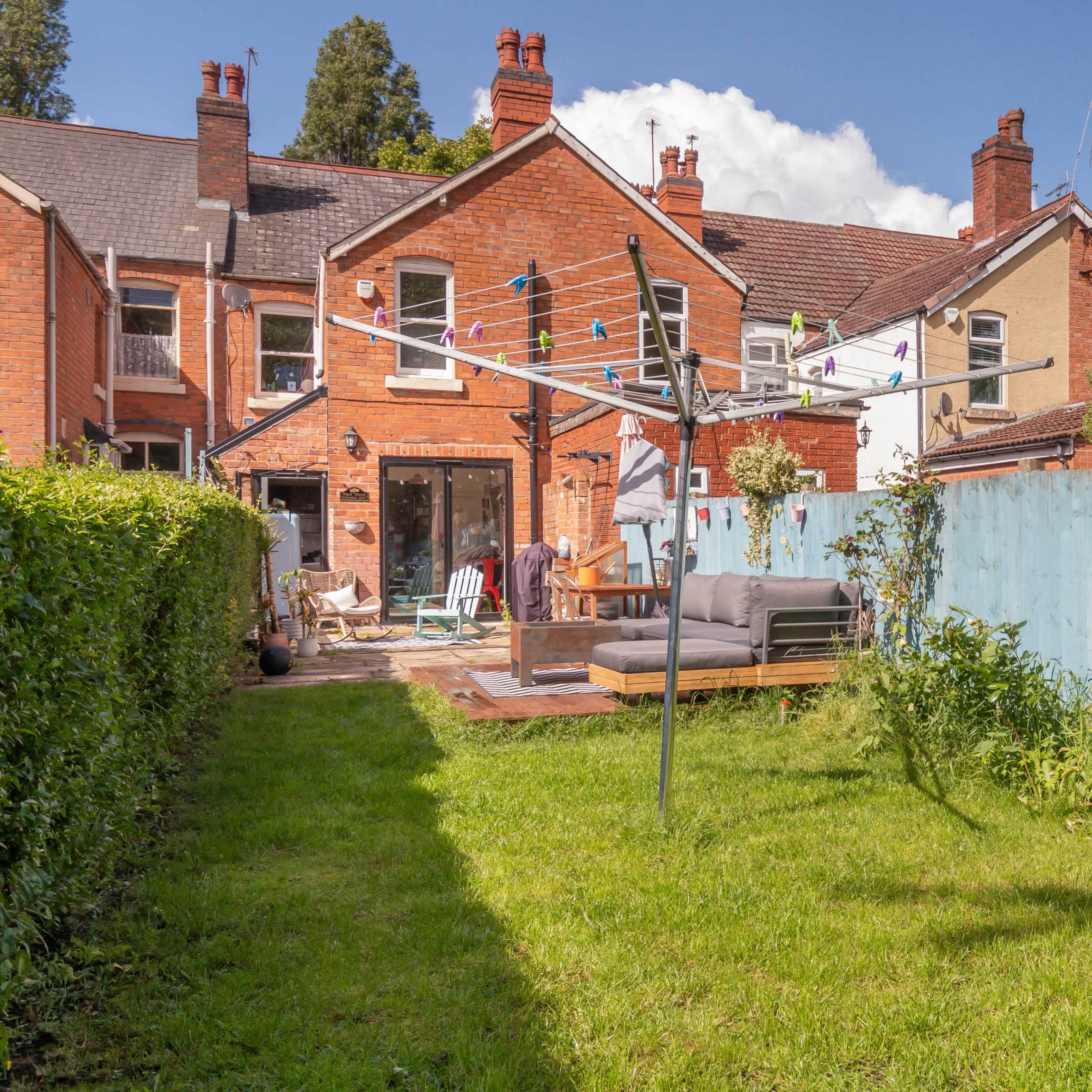 A backyard with a clothesline, a seating area, and several houses in the background, separated by a blue fence.