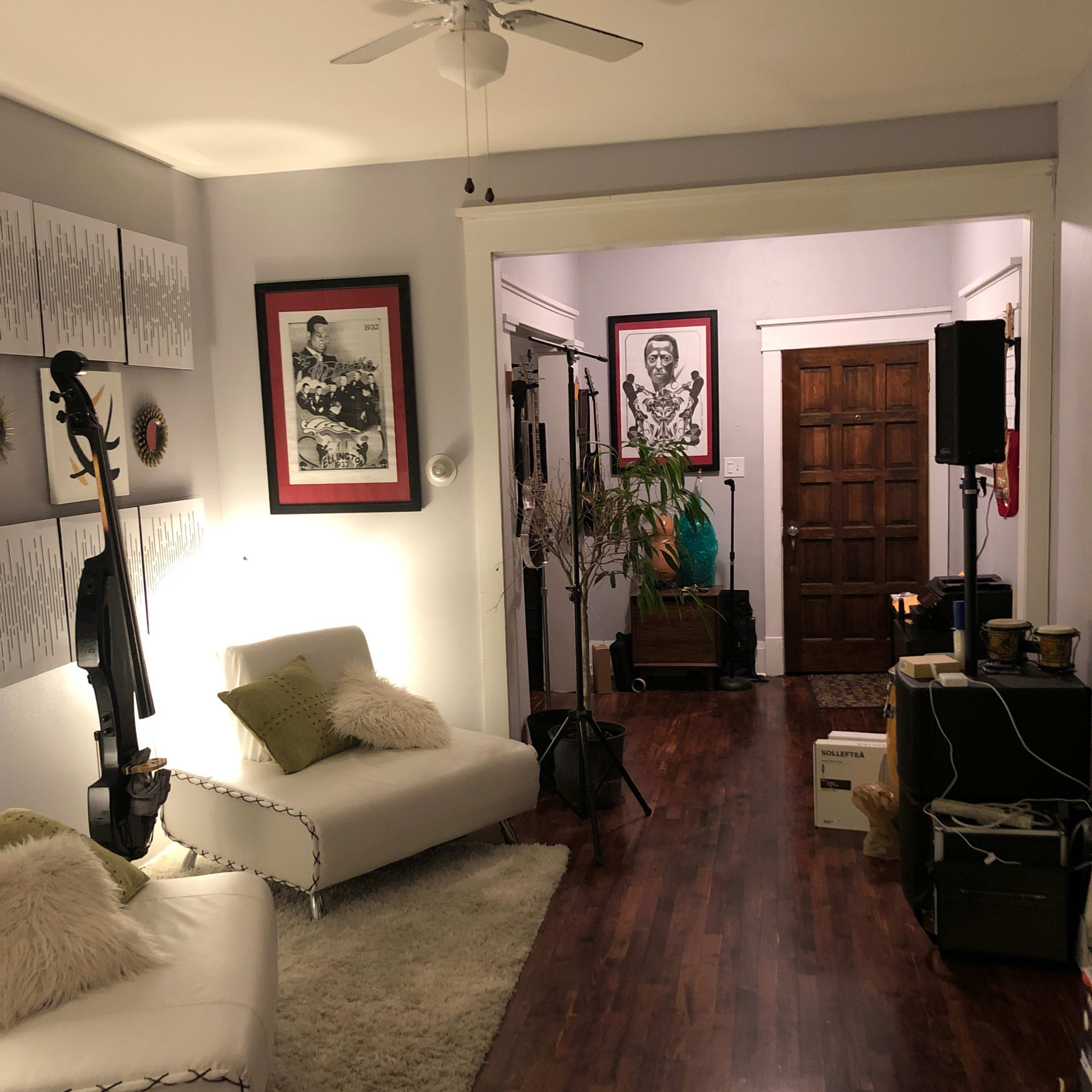 A living room with a white sofa, a ceiling fan, and a hallway leading to another room with wooden doors and framed art on the walls.
