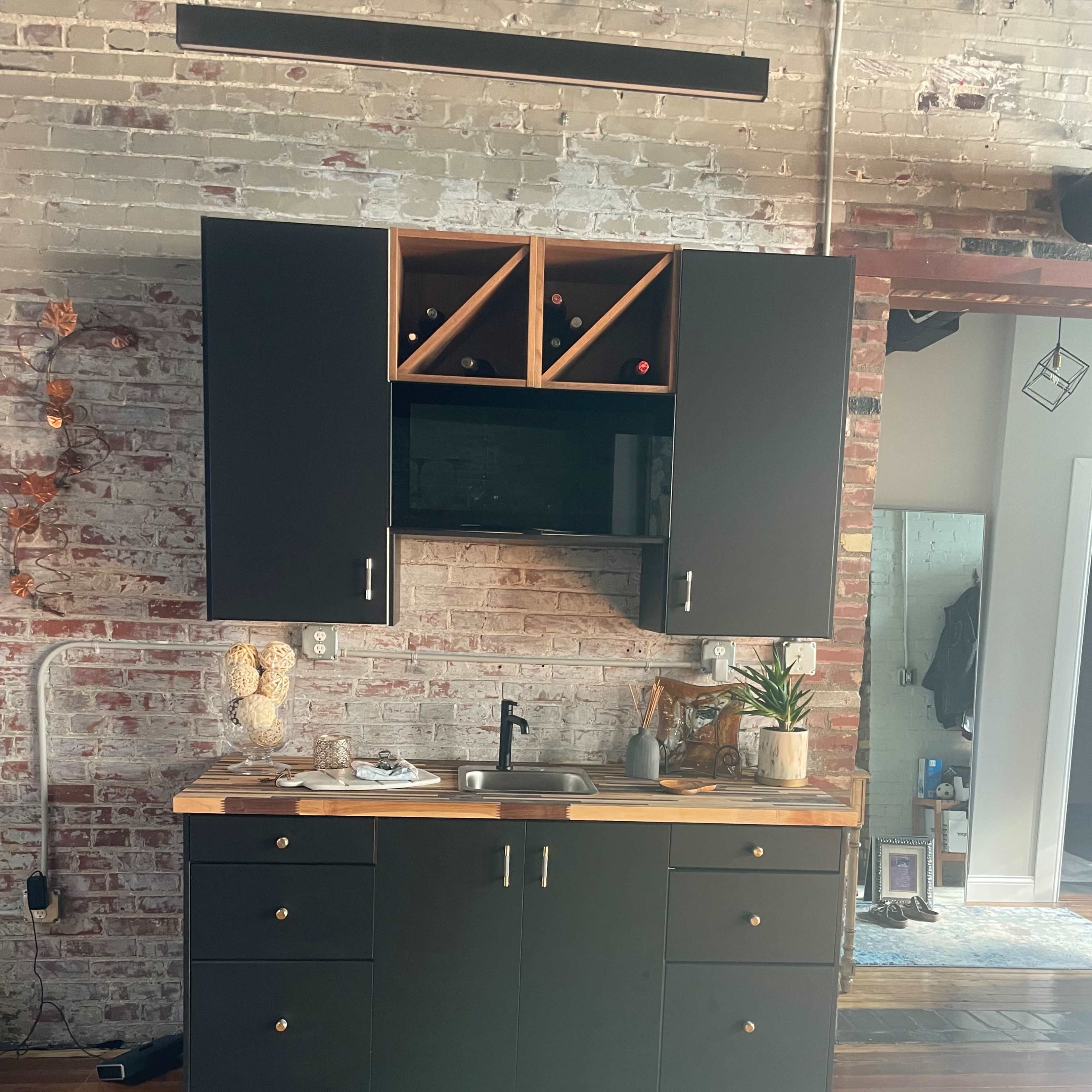 A modern kitchen area featuring dark cabinets with a wooden countertop, a wine rack, and a patterned rug on a wooden floor.