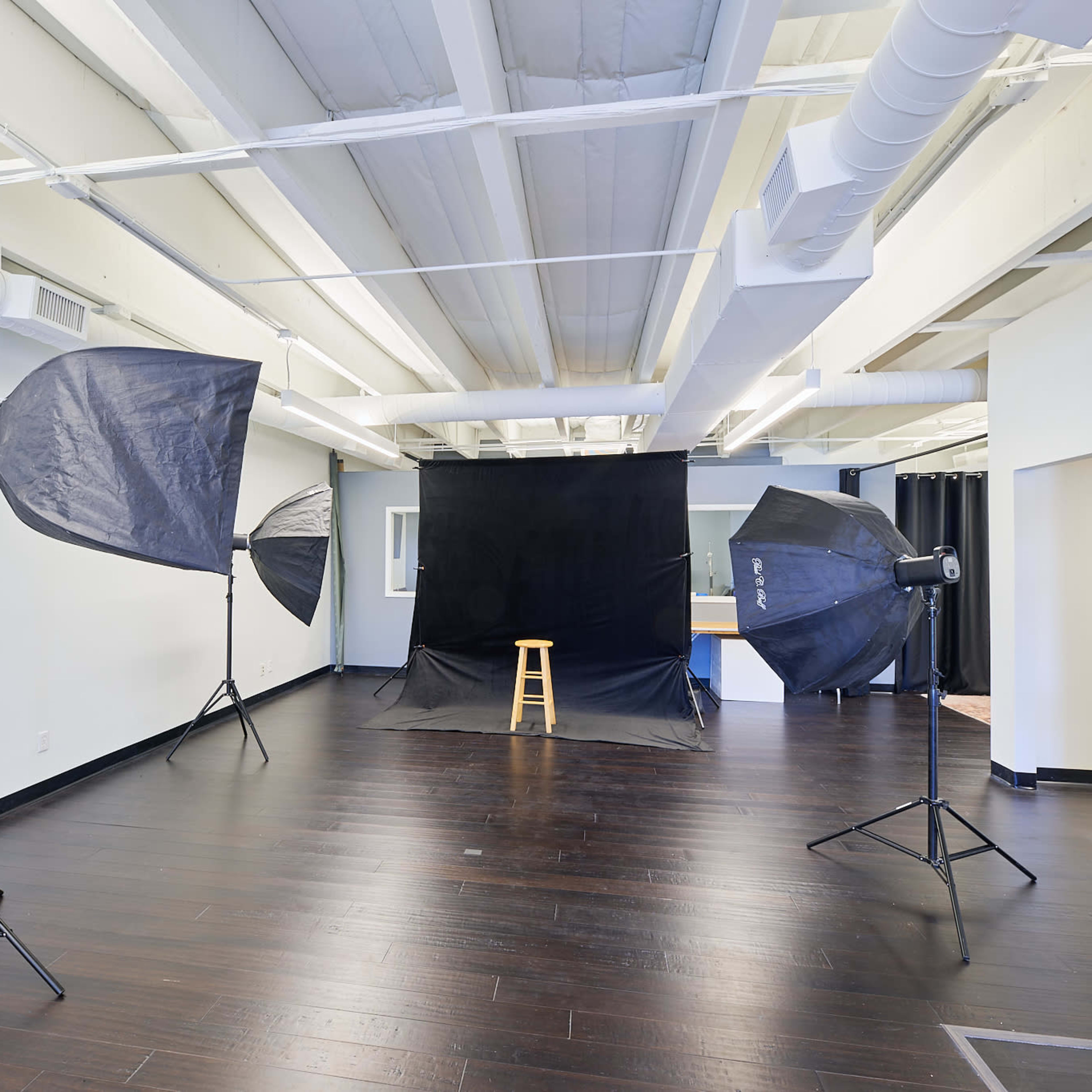 A photography studio with a black backdrop, a wooden stool, and two large softboxes positioned on either side.