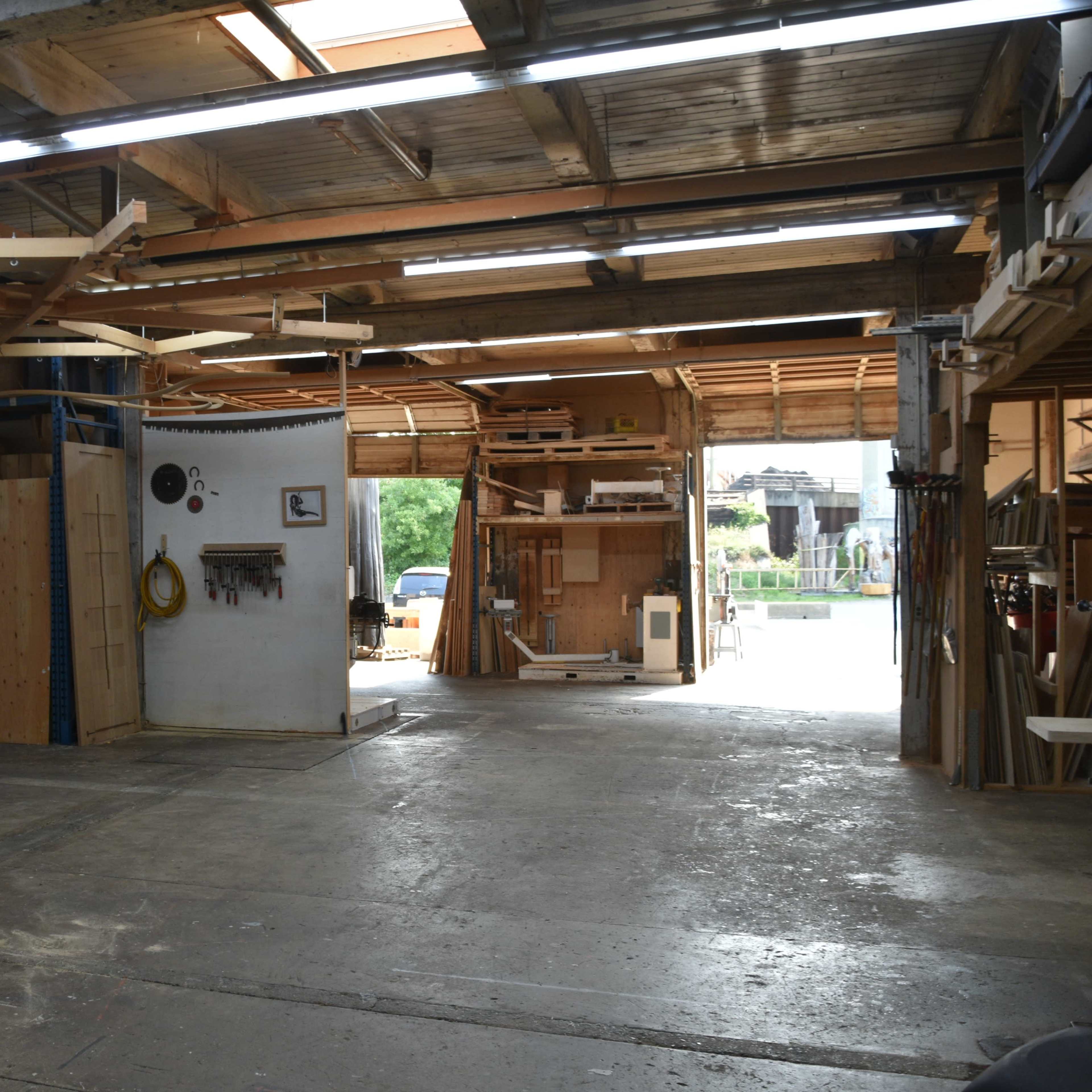 A spacious workshop with wooden shelves and tools, leading to a large open entrance.
