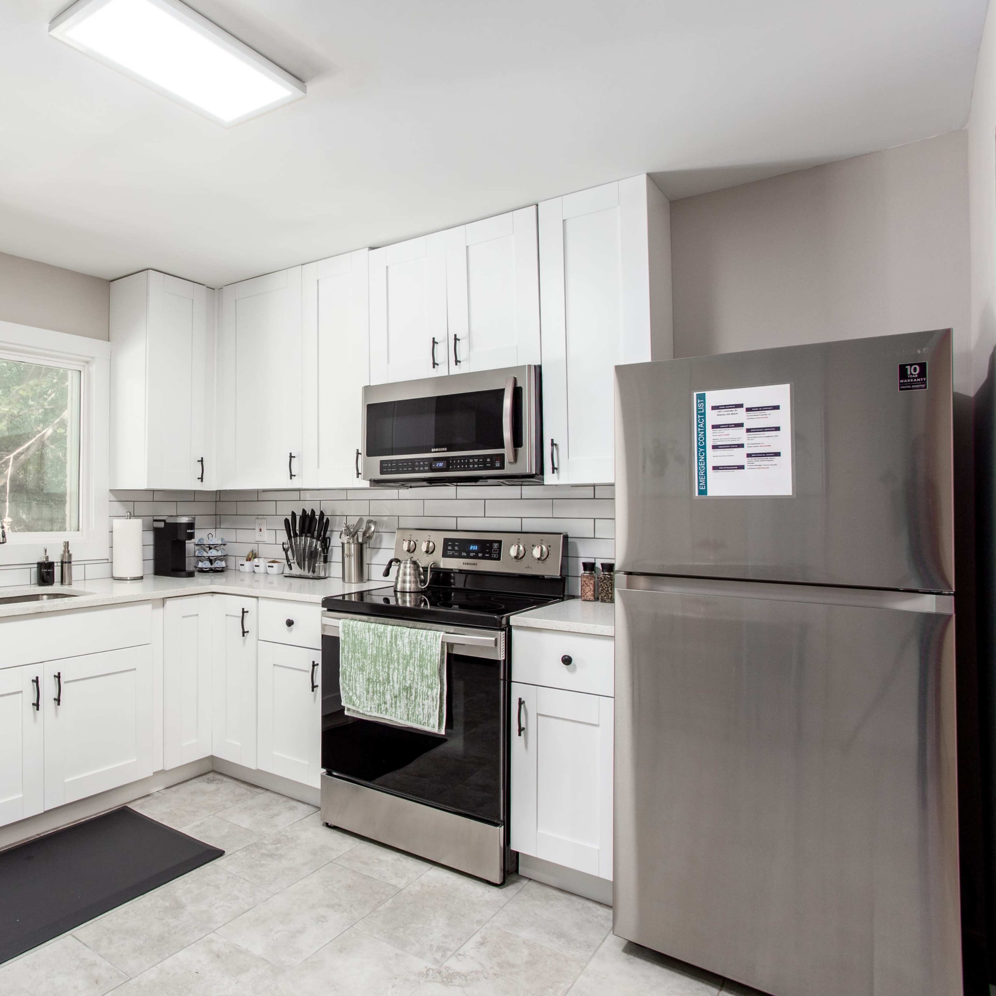 A modern kitchen with white cabinets, stainless steel appliances, and a window providing natural light.
