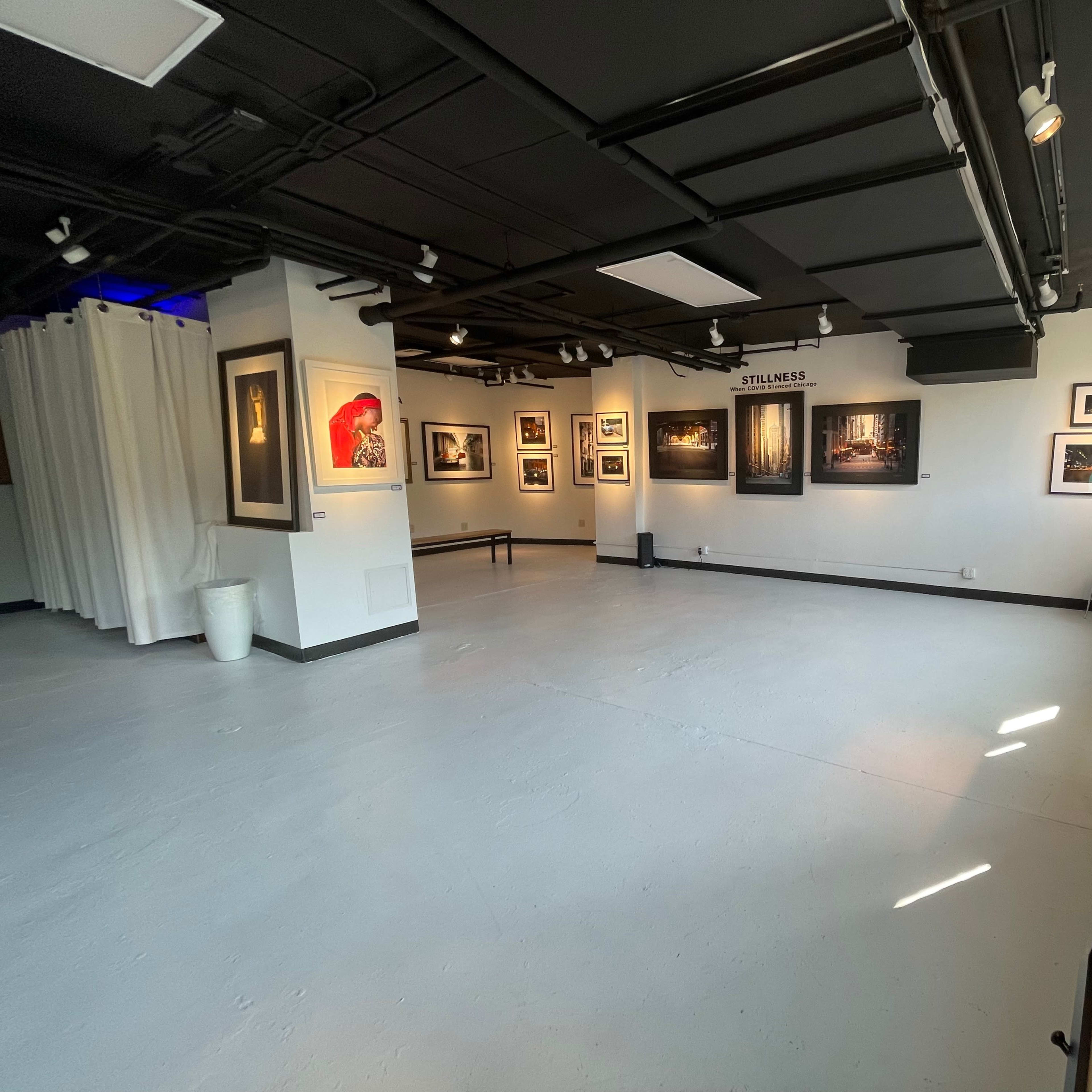 An interior view of an art gallery featuring framed photographs on white walls, with a polished concrete floor and minimalistic furniture.