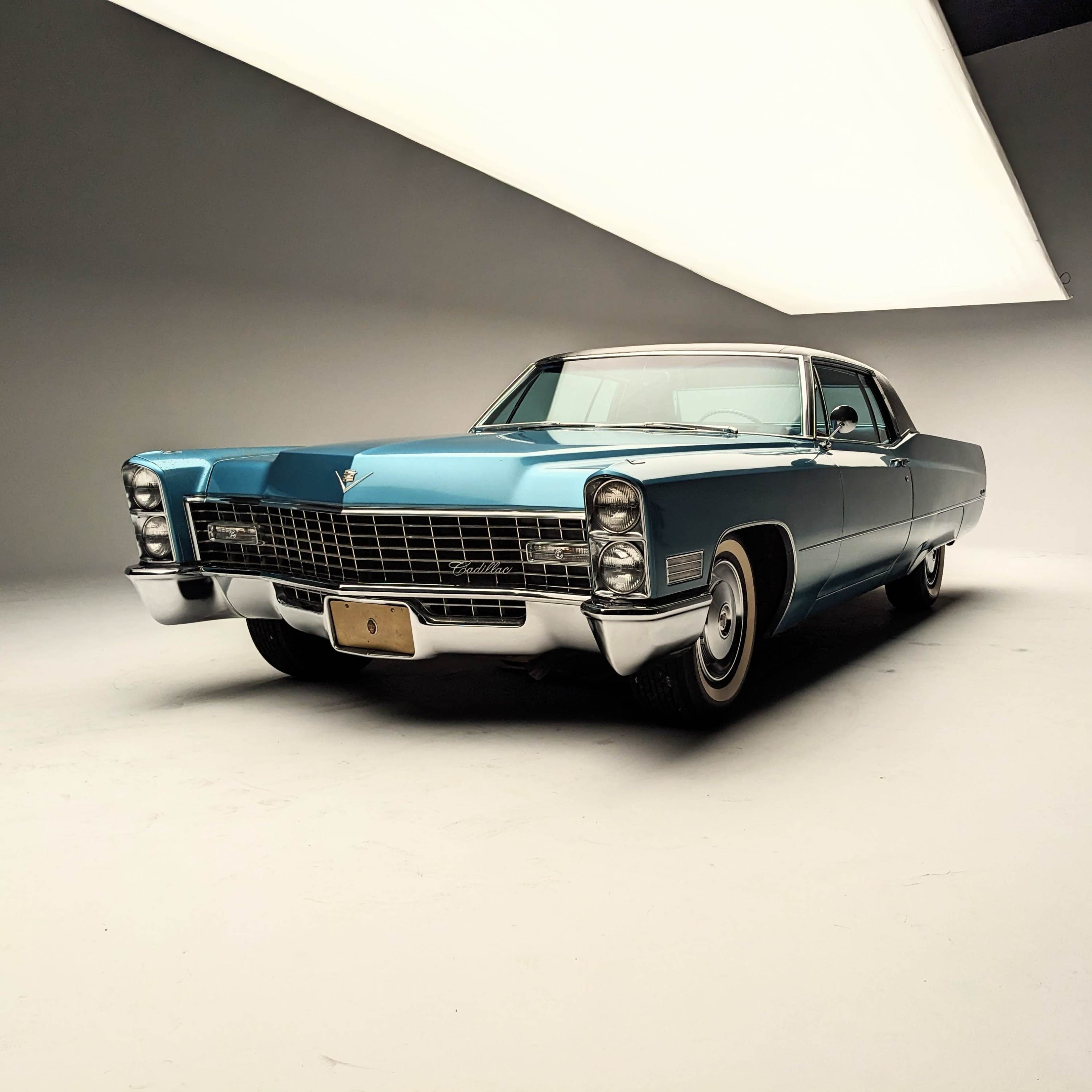 A vintage blue Cadillac parked in a well-lit studio with a minimalist backdrop.