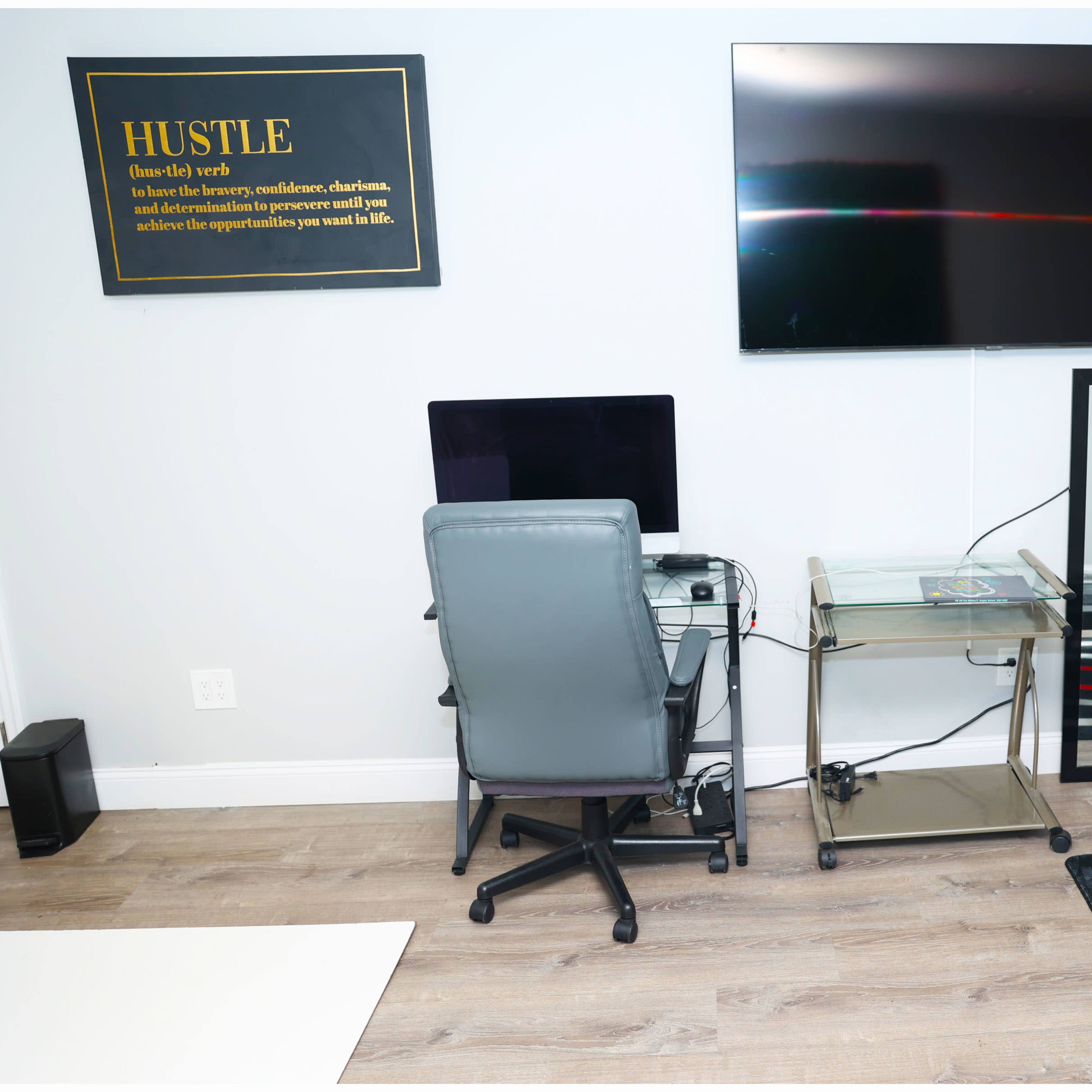 A workspace featuring a computer desk with a chair, a large wall-mounted TV, a mirror, and a coffee table with magazines on it.