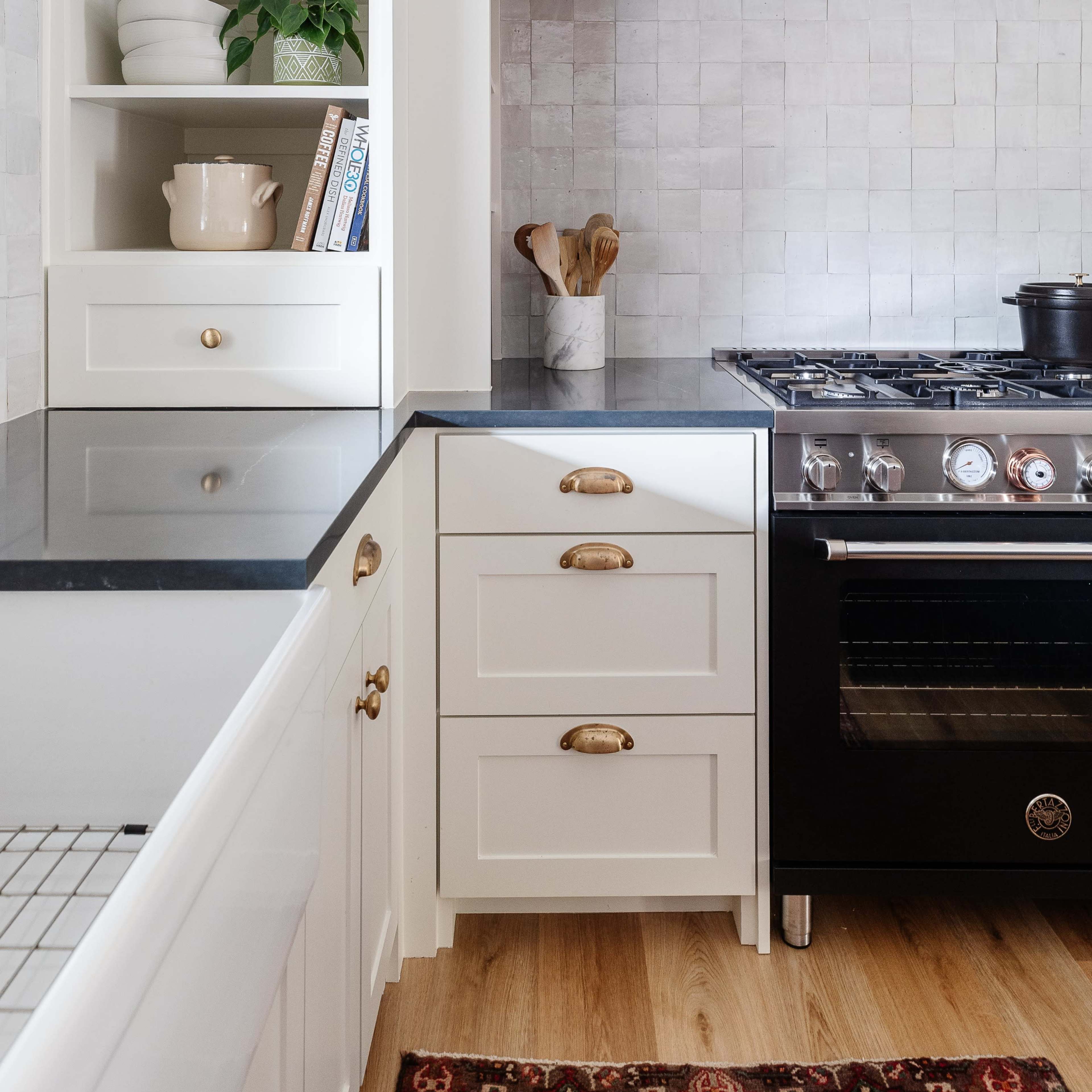 A modern kitchen features white cabinetry, a black stove, and a gray tile backsplash.