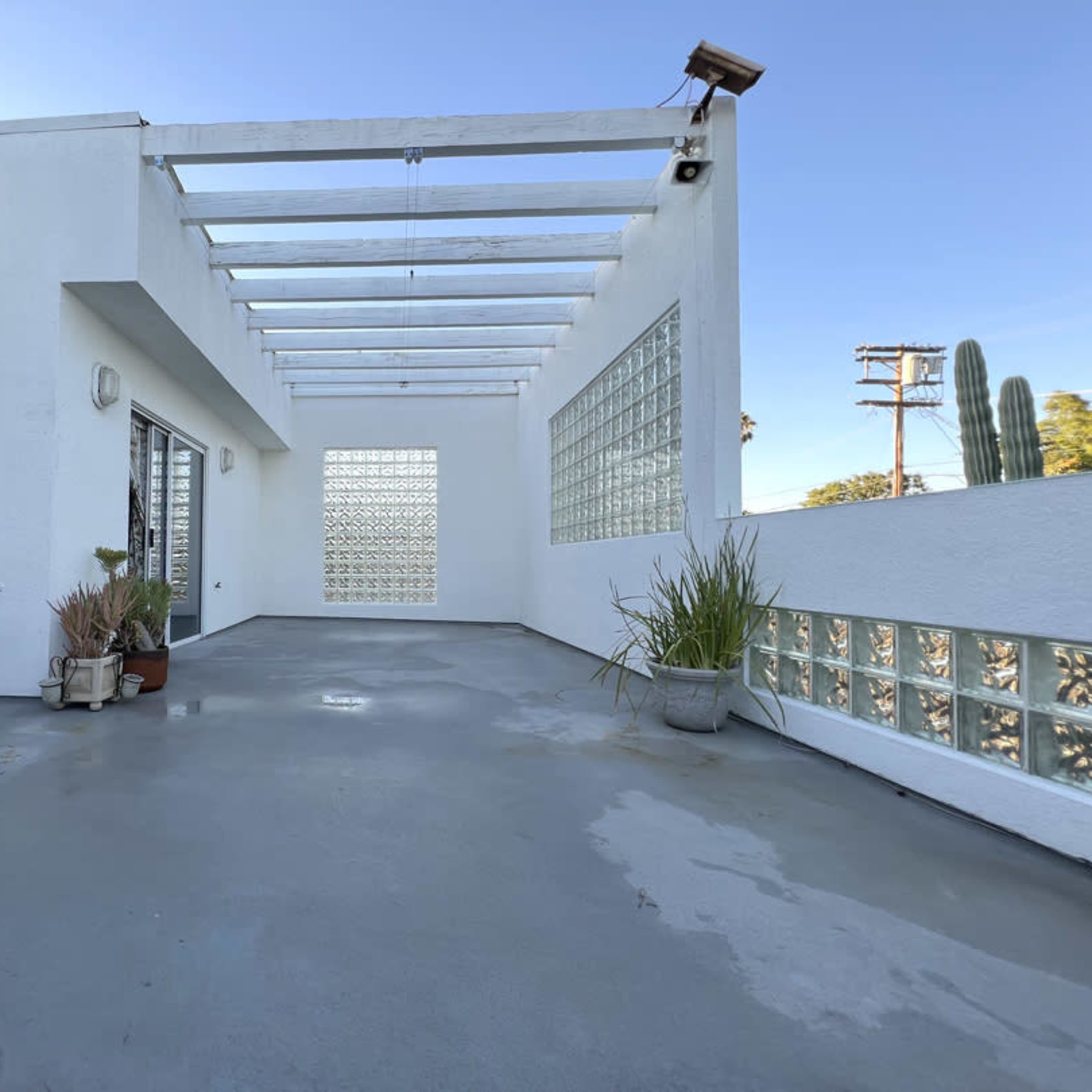 A spacious, white outdoor patio area with a glass block wall and various potted plants.
