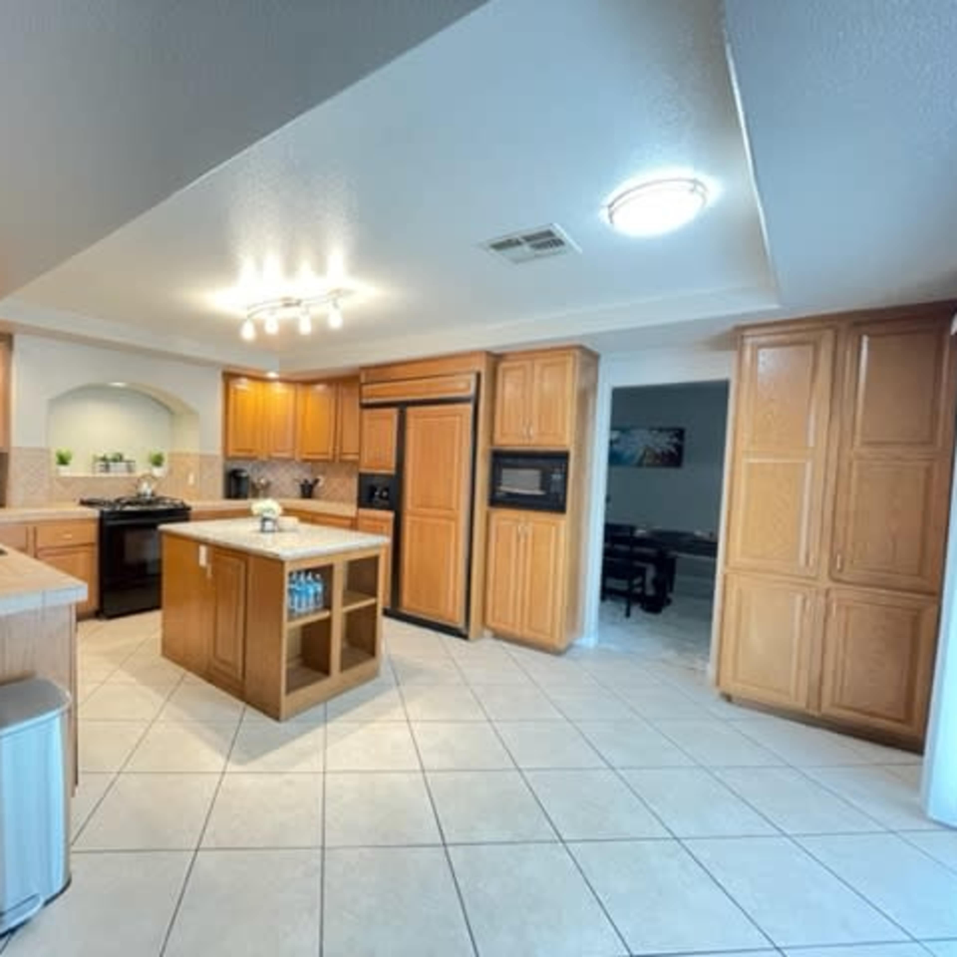 A spacious kitchen with wooden cabinetry, modern appliances, and a light-colored tile floor.