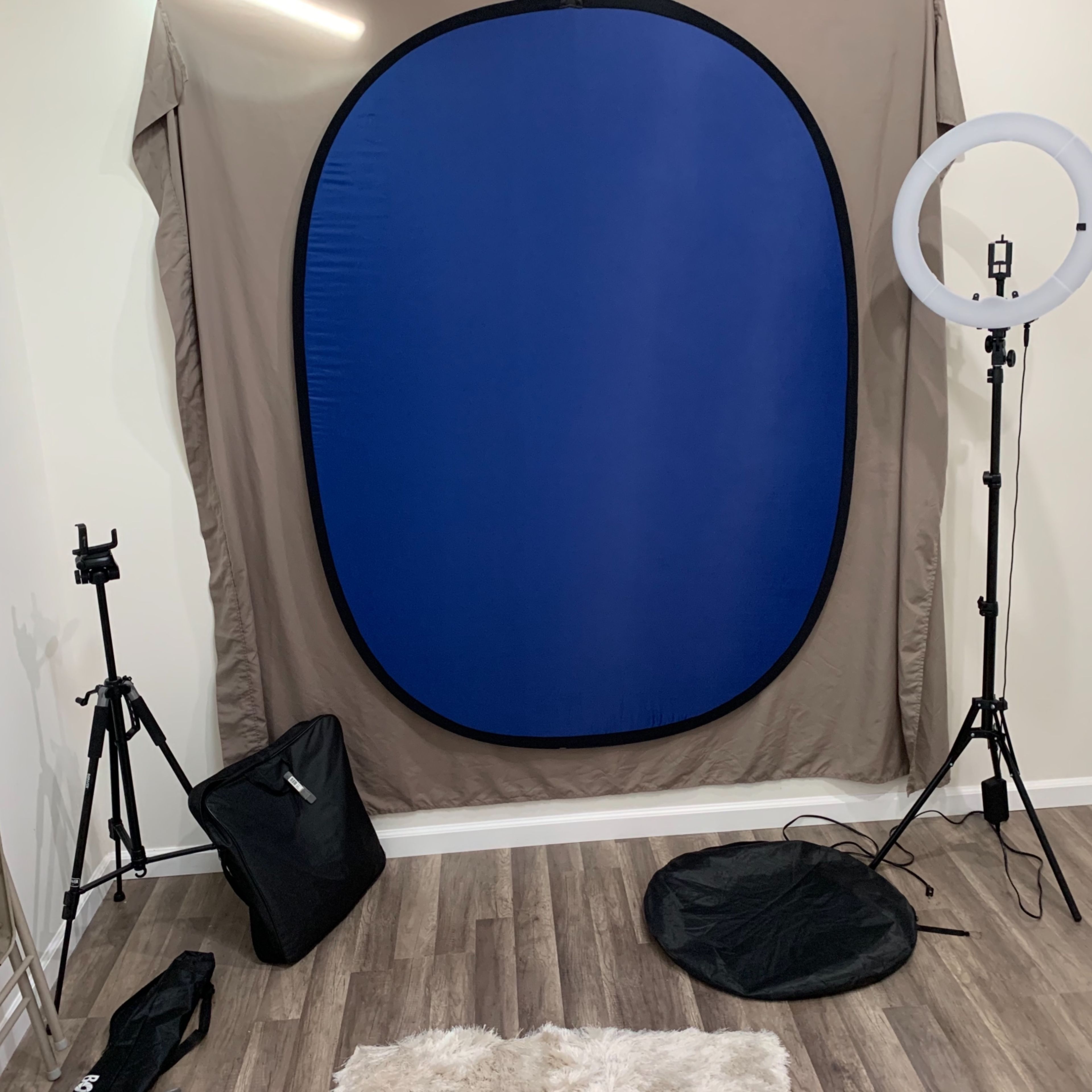 A photography setup featuring a blue backdrop, a ring light on a stand, and tripods in a room with hardwood flooring.