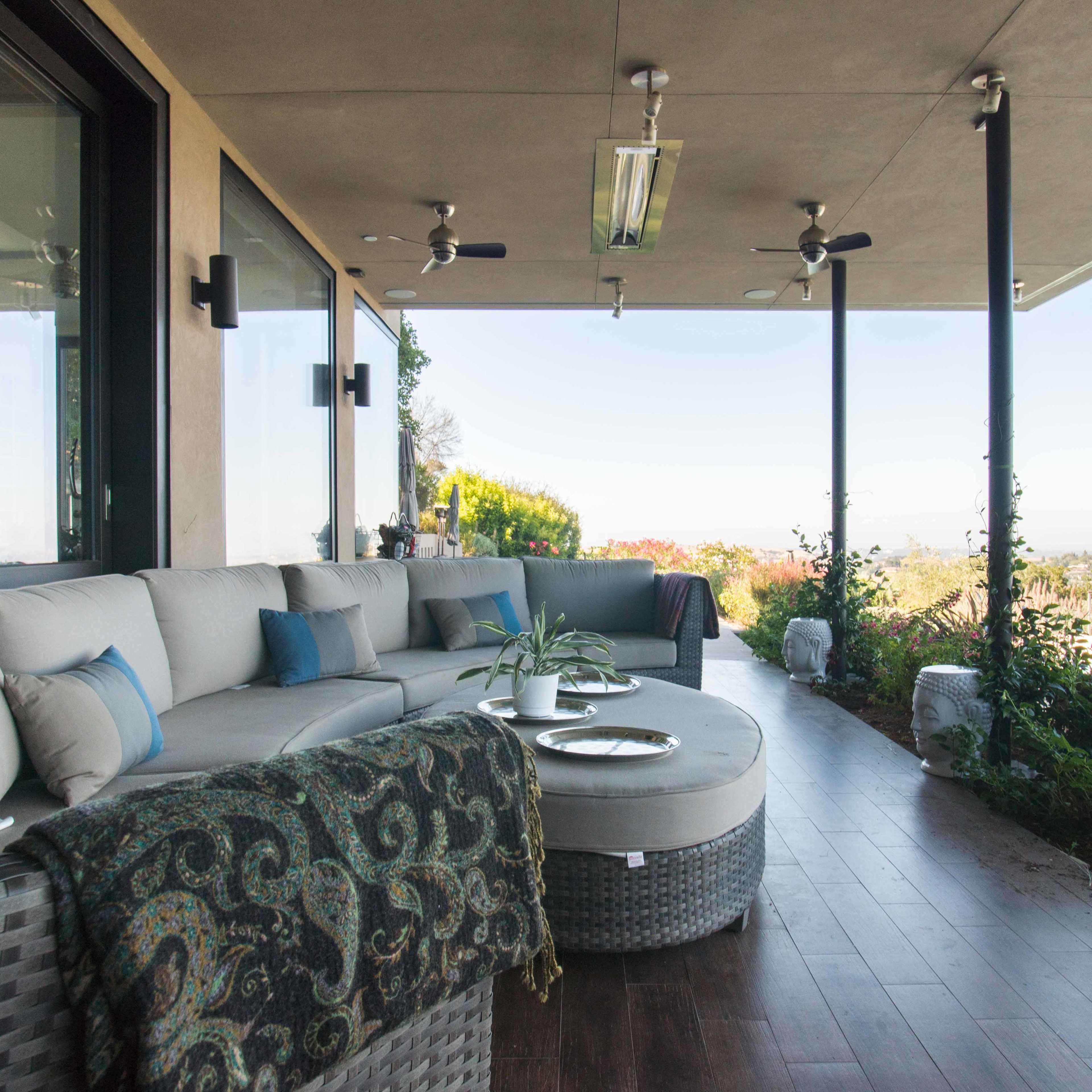 A modern outdoor patio with a large sectional sofa, decorative pillows, and a coffee table, overlooking a landscape and pool.