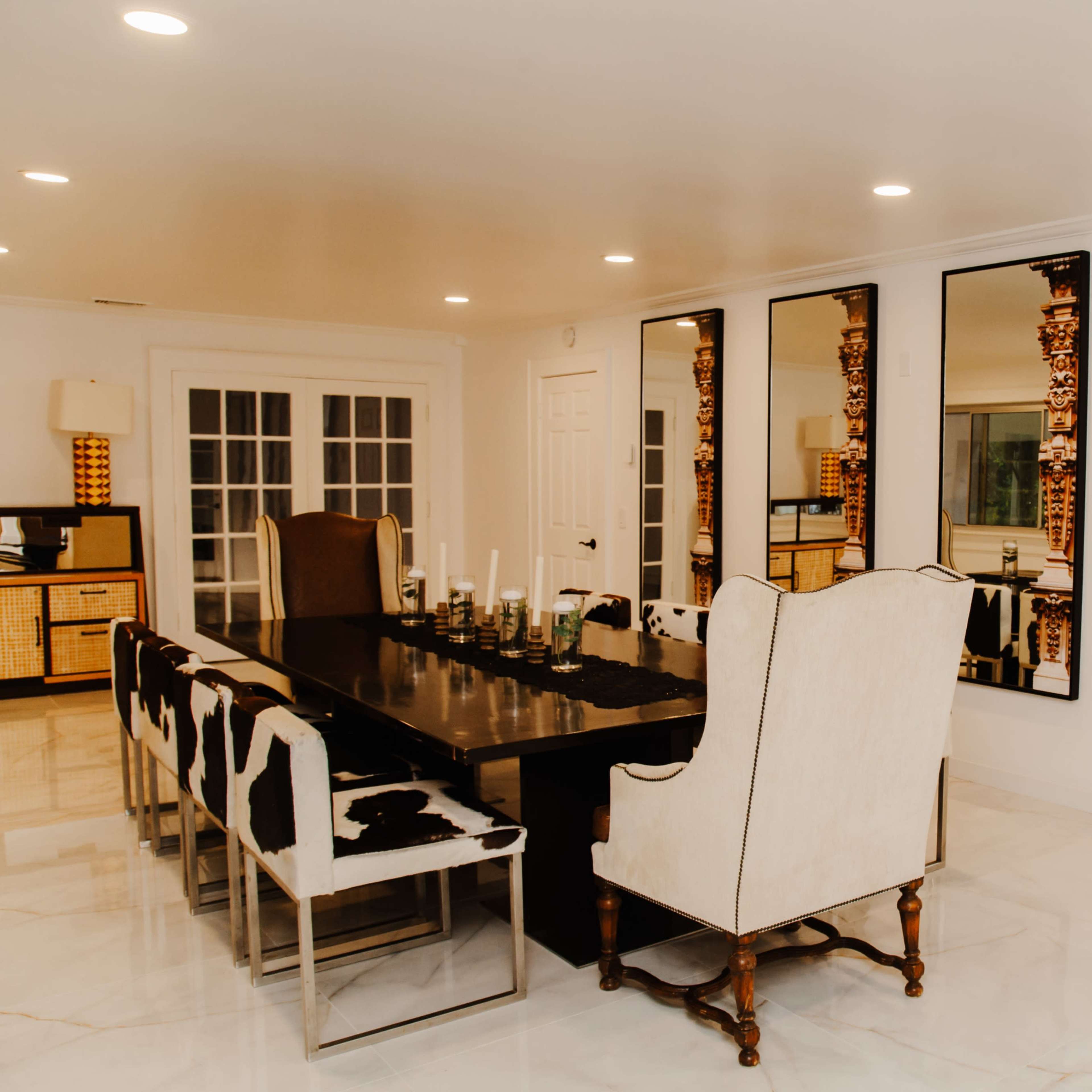 The dining room features a long black table surrounded by patterned chairs and large mirrors on the wall reflecting the space.