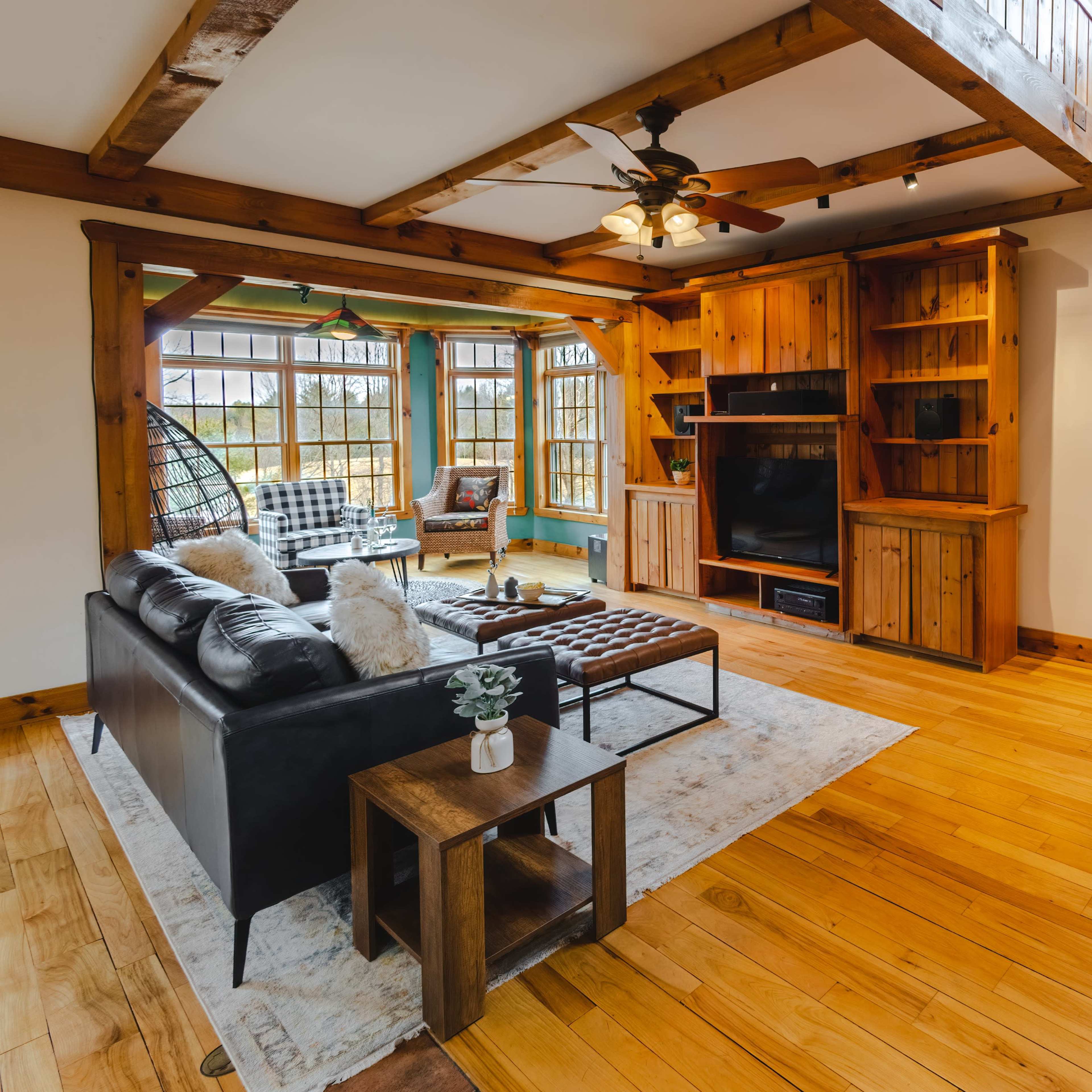 A cozy living room with a wooden ceiling, a black leather sofa, a coffee table, built-in shelves, and a fireplace.