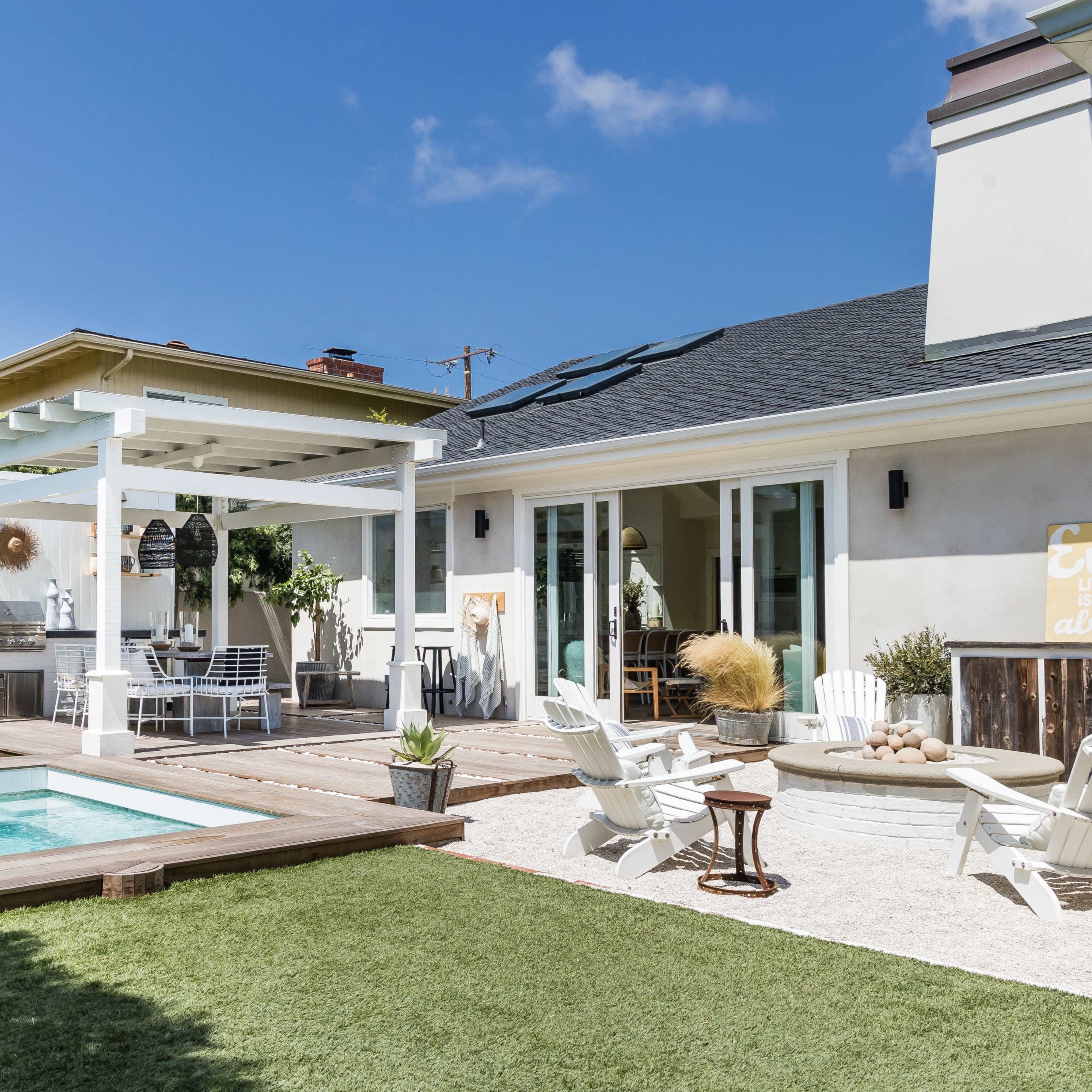 A backyard with a swimming pool, outdoor seating area, and a covered pergola, surrounded by green grass and landscaping.