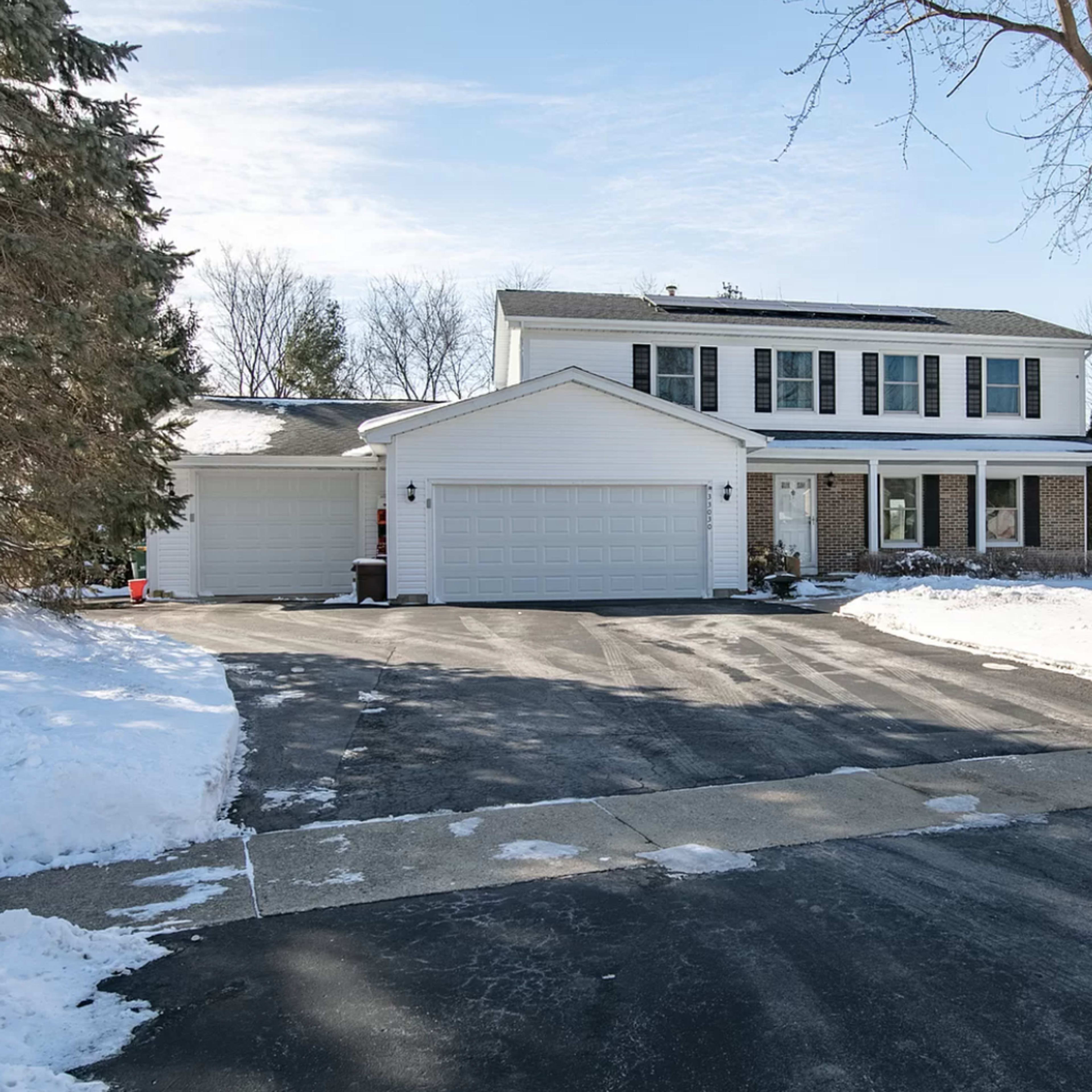 A two-story house with a spacious driveway and snow-covered landscaping is shown.