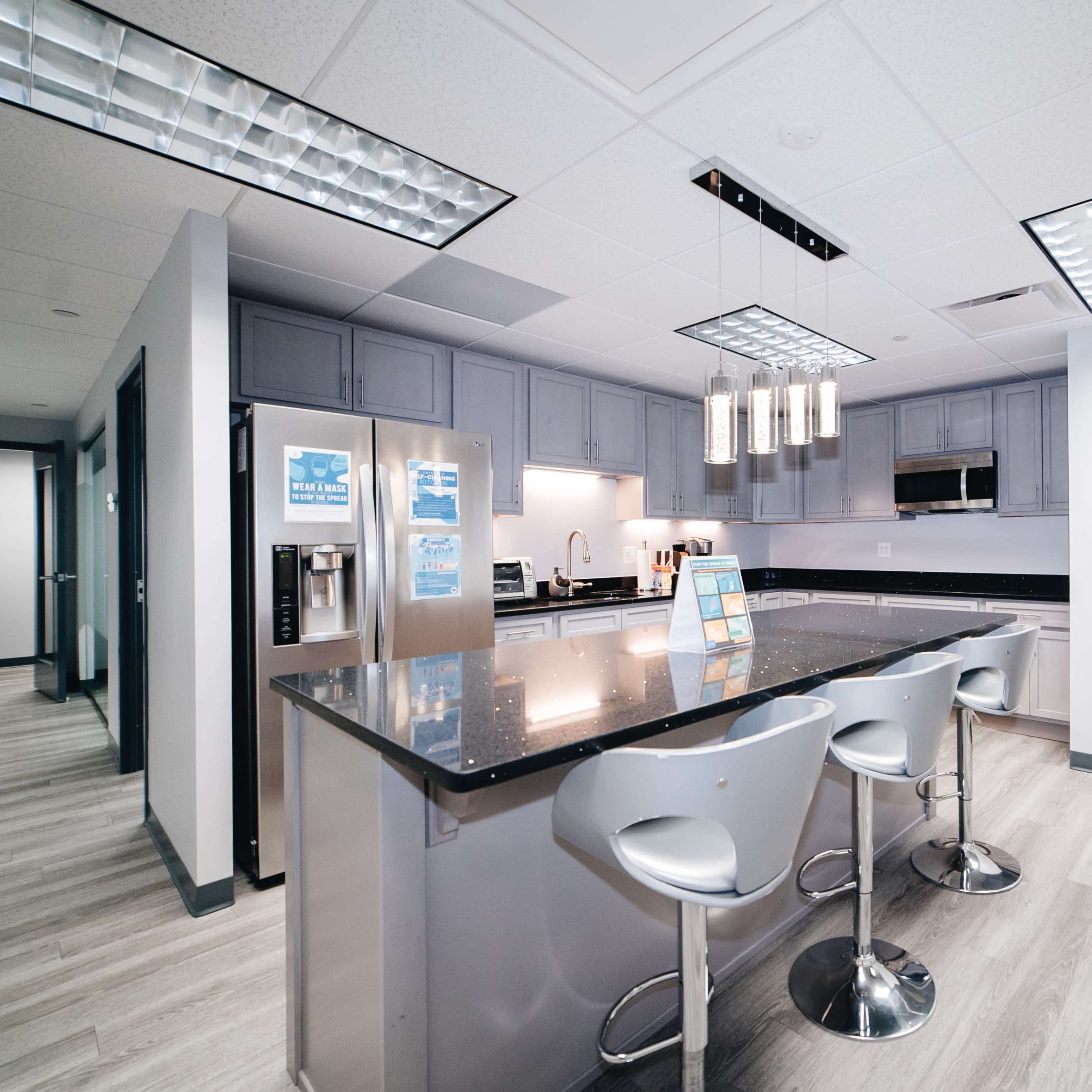 The kitchen features modern gray cabinetry, a large island with seating, and stainless steel appliances.