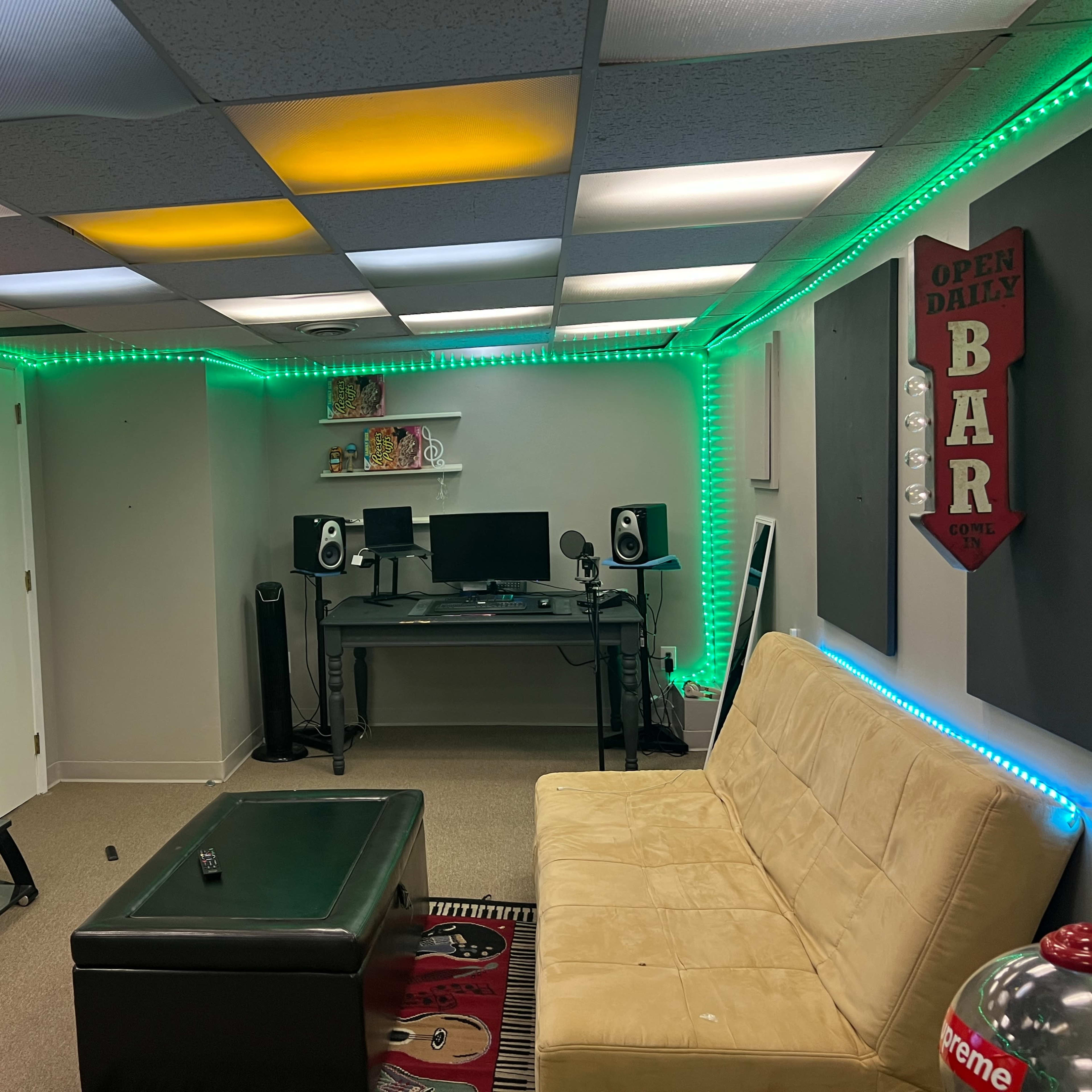 A cozy room featuring a couch, a coffee table, a television, and a desk with computer equipment, all illuminated by colorful LED lights along the walls and ceiling.