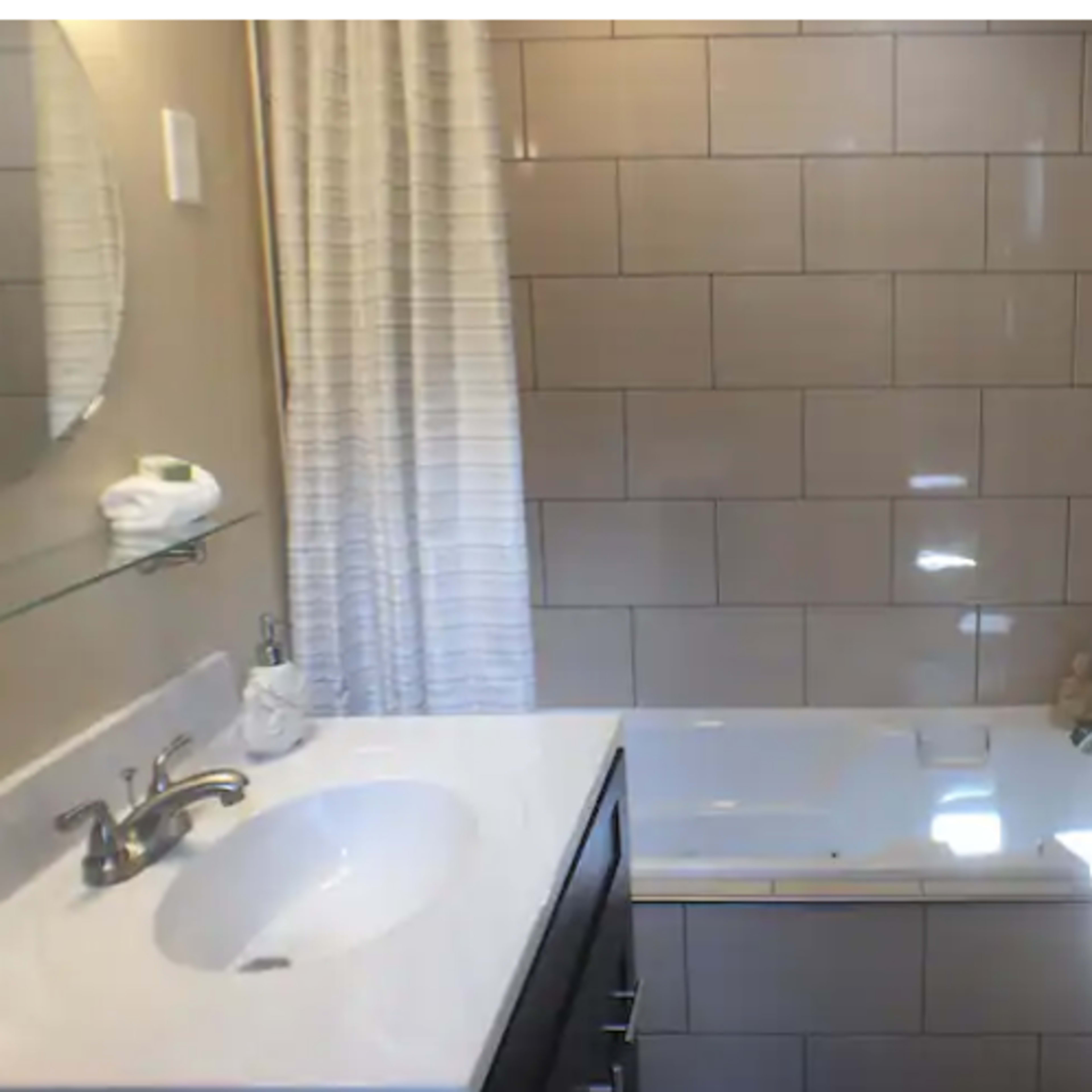 A modern bathroom featuring a bathtub, sink with a mirror, and a shower area with tiled walls.