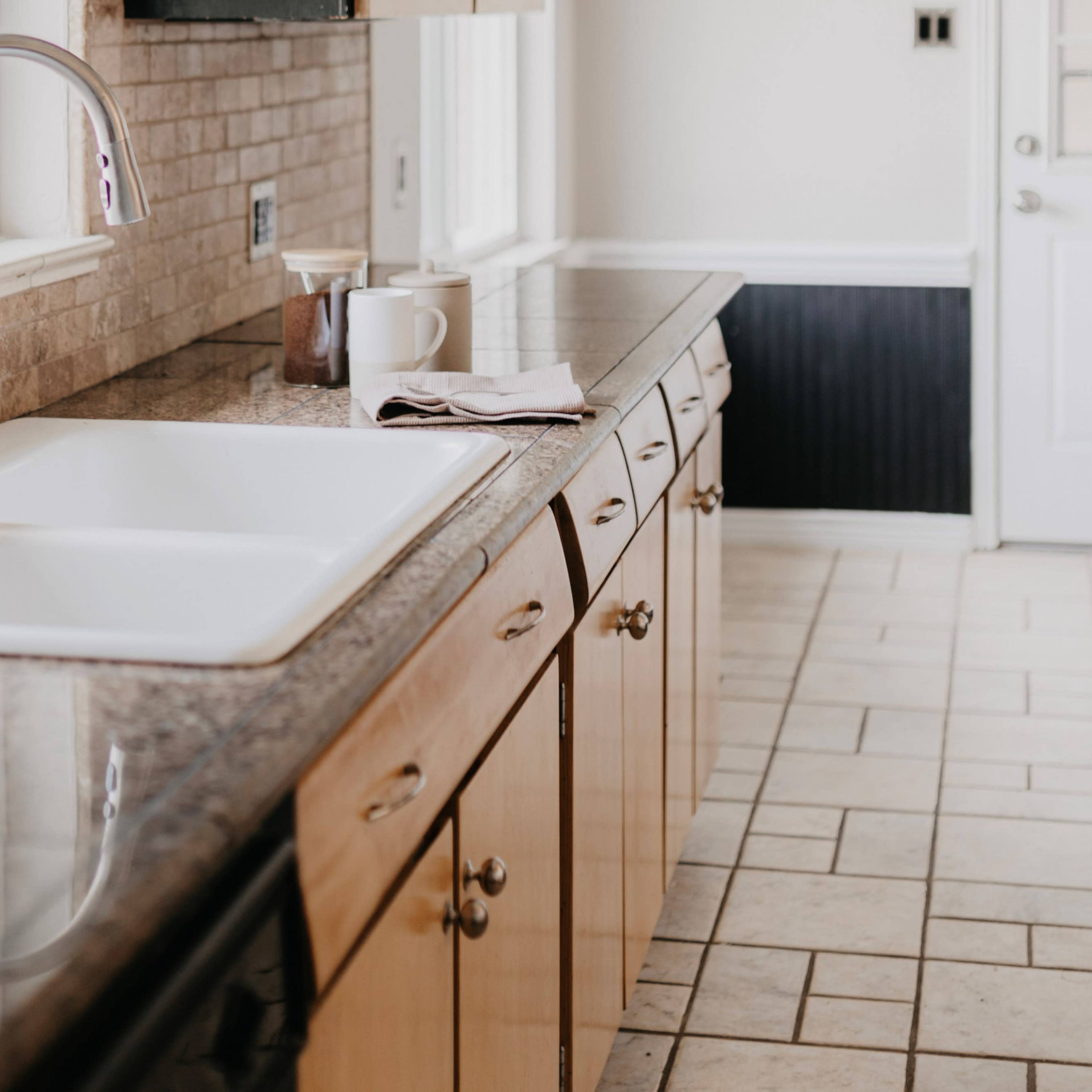 A modern kitchen with a stone countertop, a white sink, wooden cabinets, and a tiled floor.
