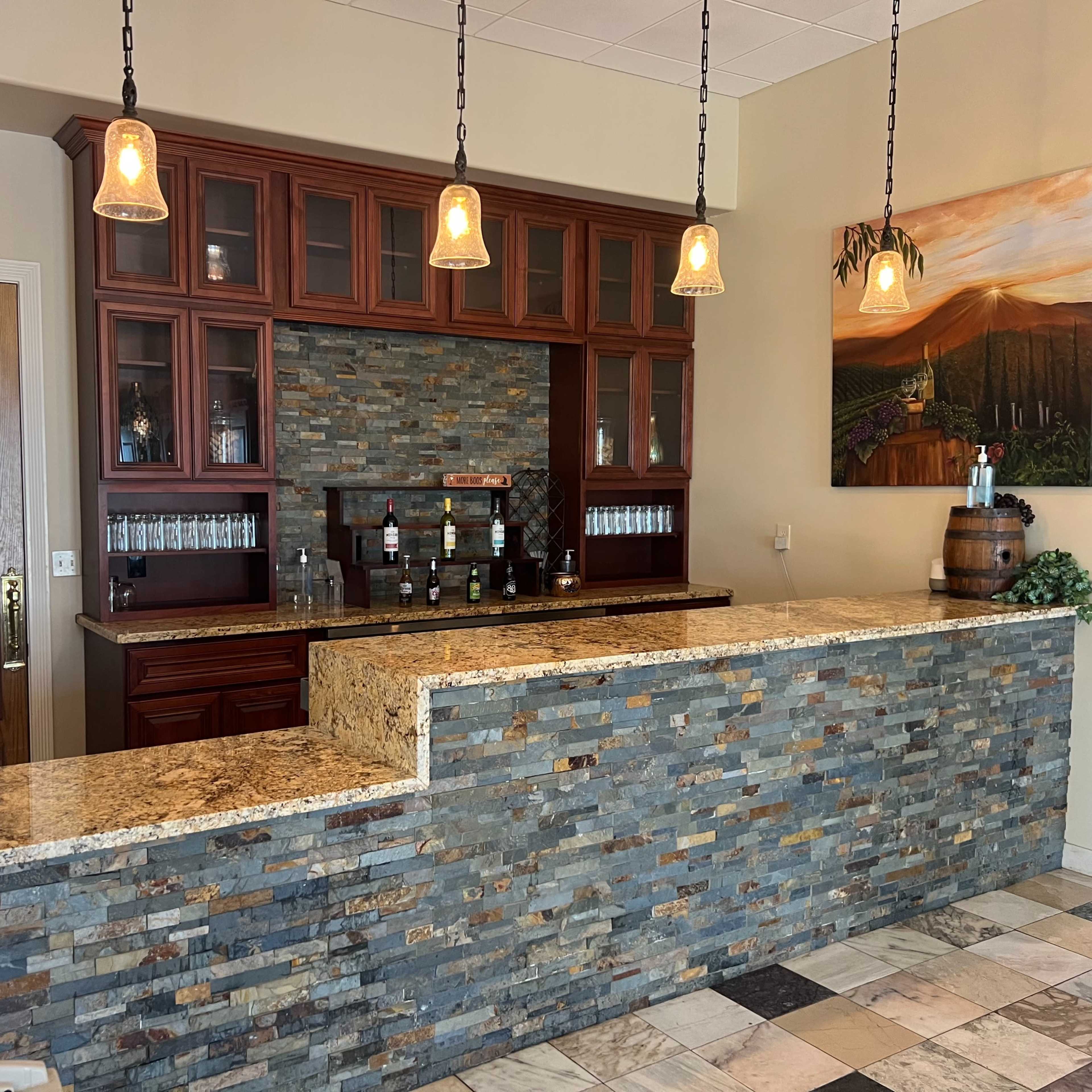 A modern bar area with a stone countertop, wooden cabinetry, and pendant lights hanging above.