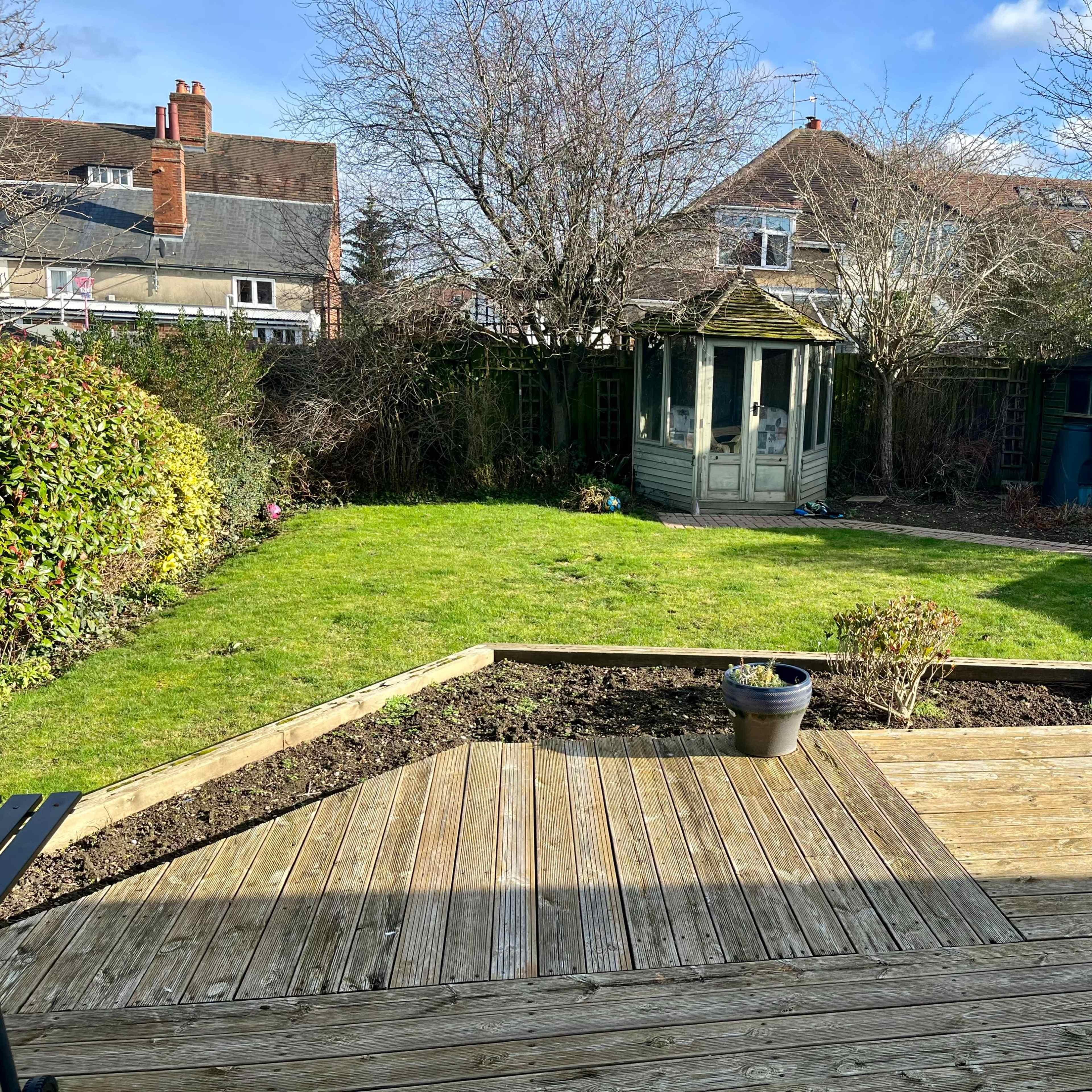 A well-maintained garden featuring a wooden deck, a central lawn, a gazebo, and surrounding trees and shrubs.