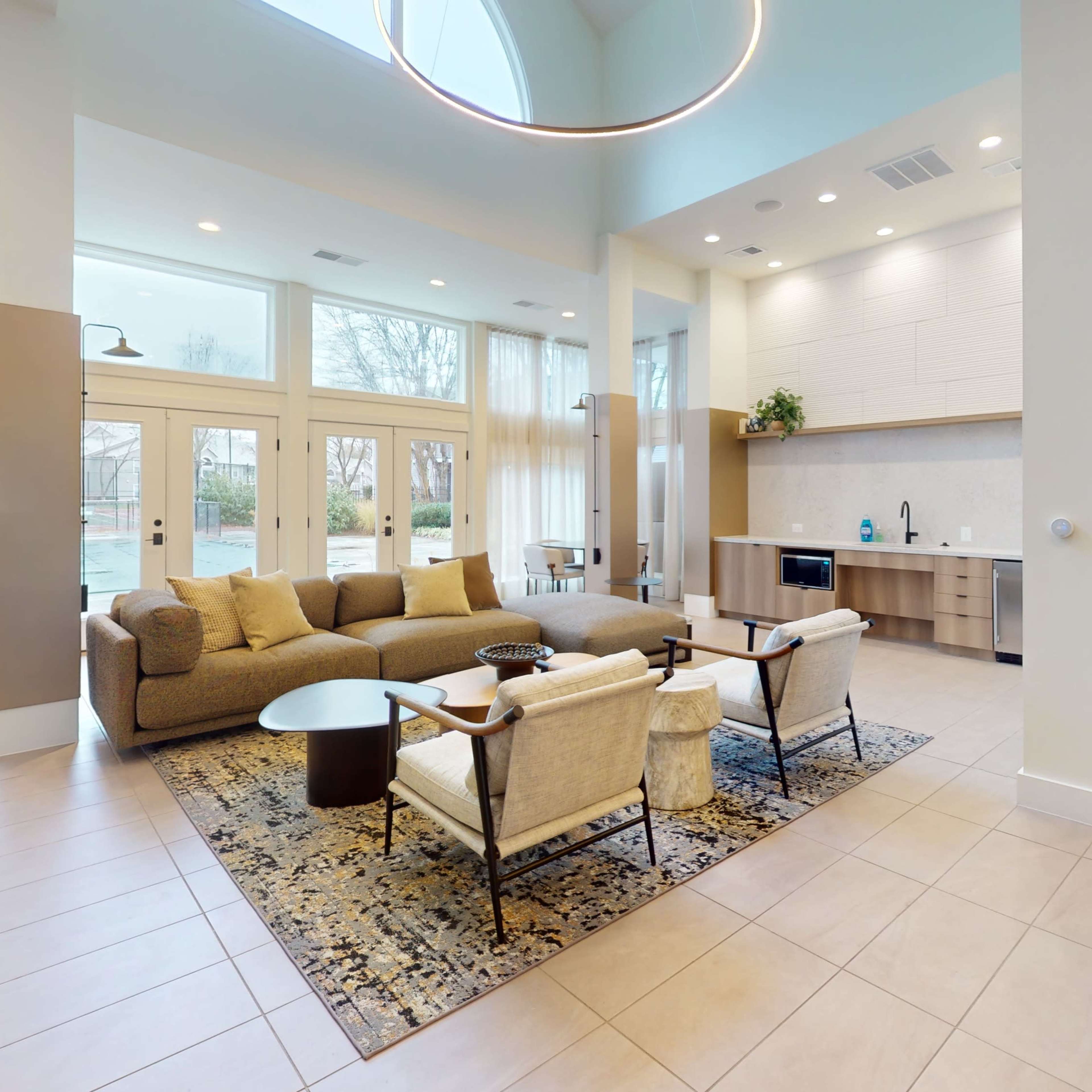 A modern lounge area with a light-colored sofa, armchairs, a round coffee table, and large windows allowing natural light to fill the space.
