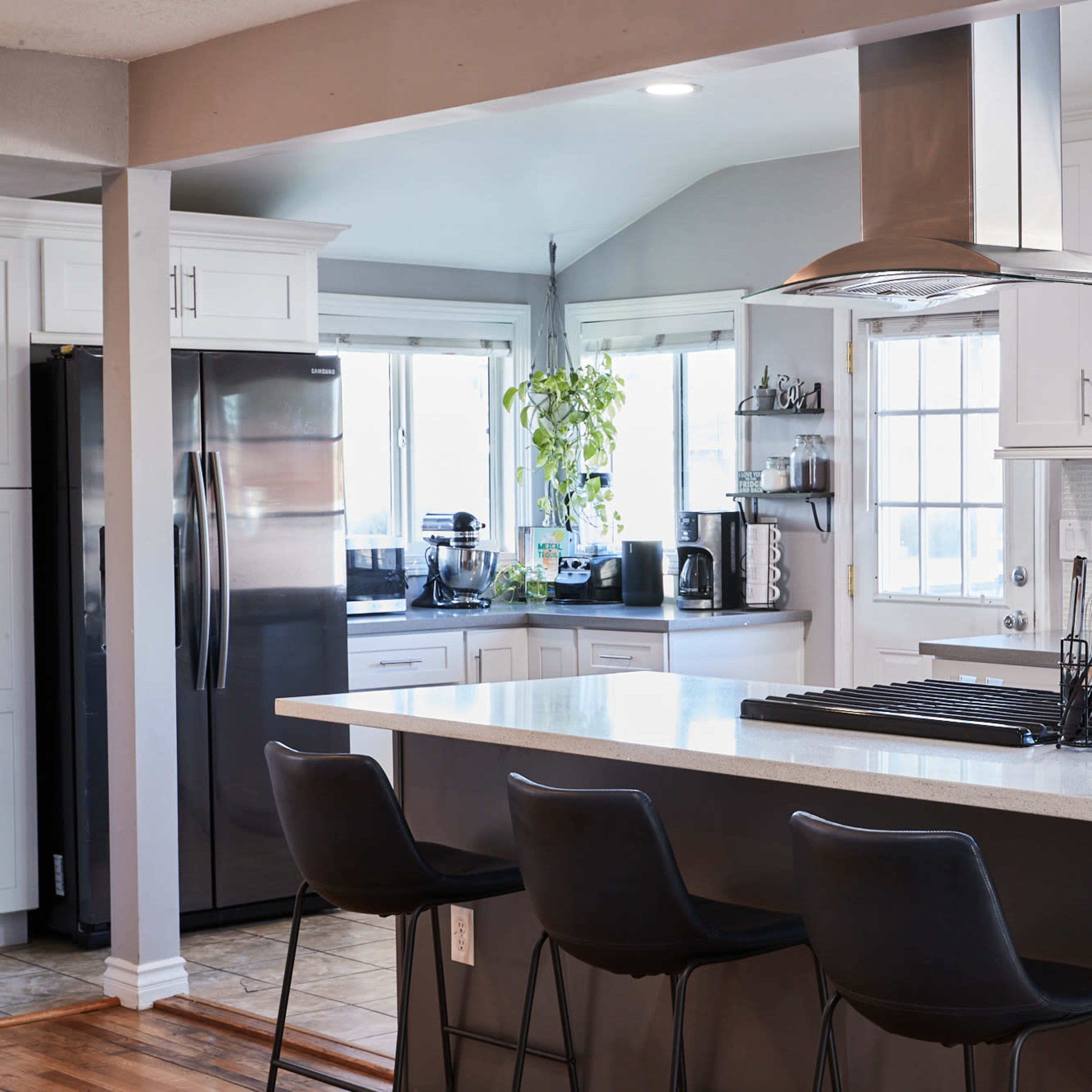A modern kitchen with white cabinets, a large island with bar stools, and stainless steel appliances.
