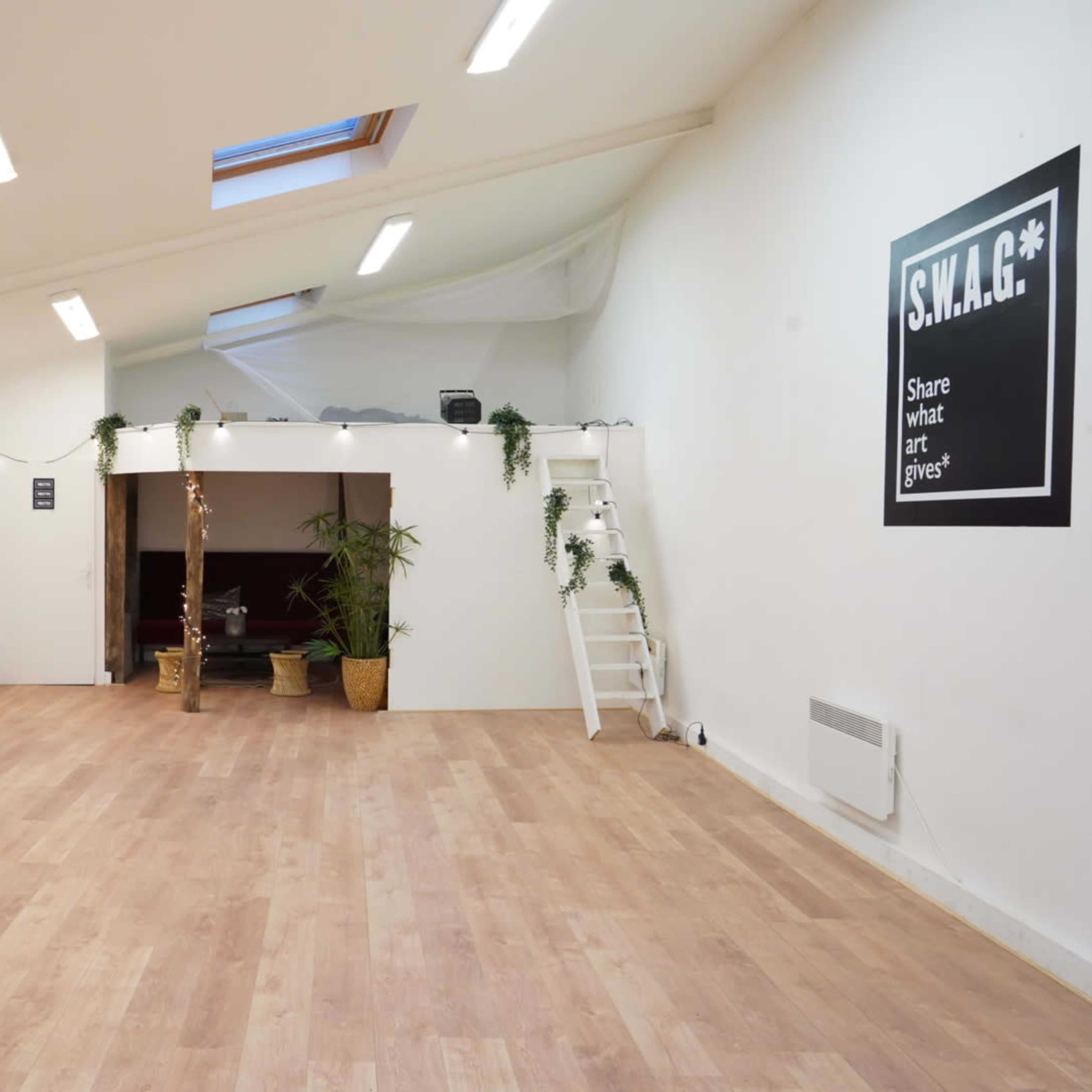 The interior of a spacious, well-lit studio features a mirrored wall, potted plants, and a sign that reads "S.W.A.G.*" on one side.