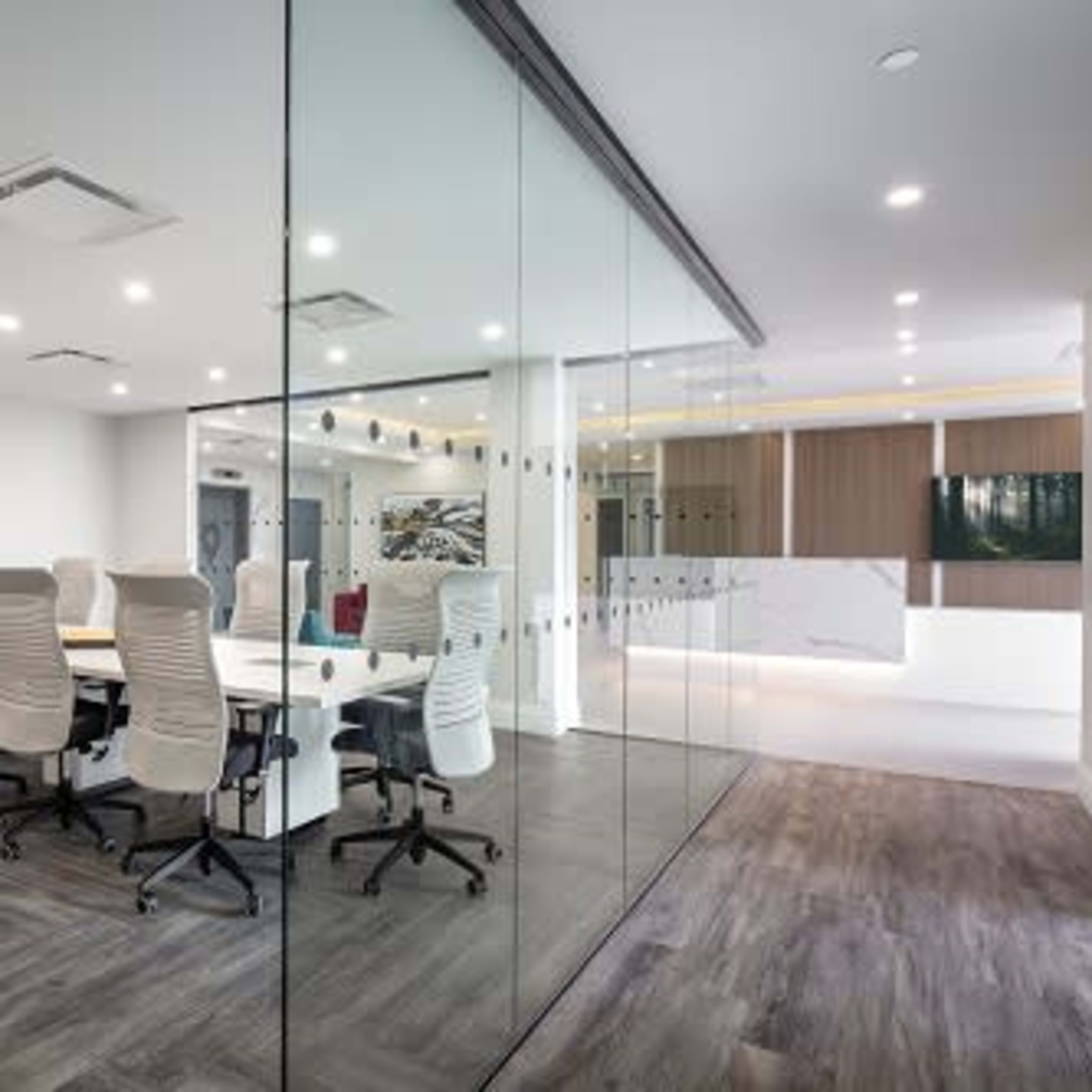 A modern conference room with a long table surrounded by ergonomic chairs, enclosed by glass walls.