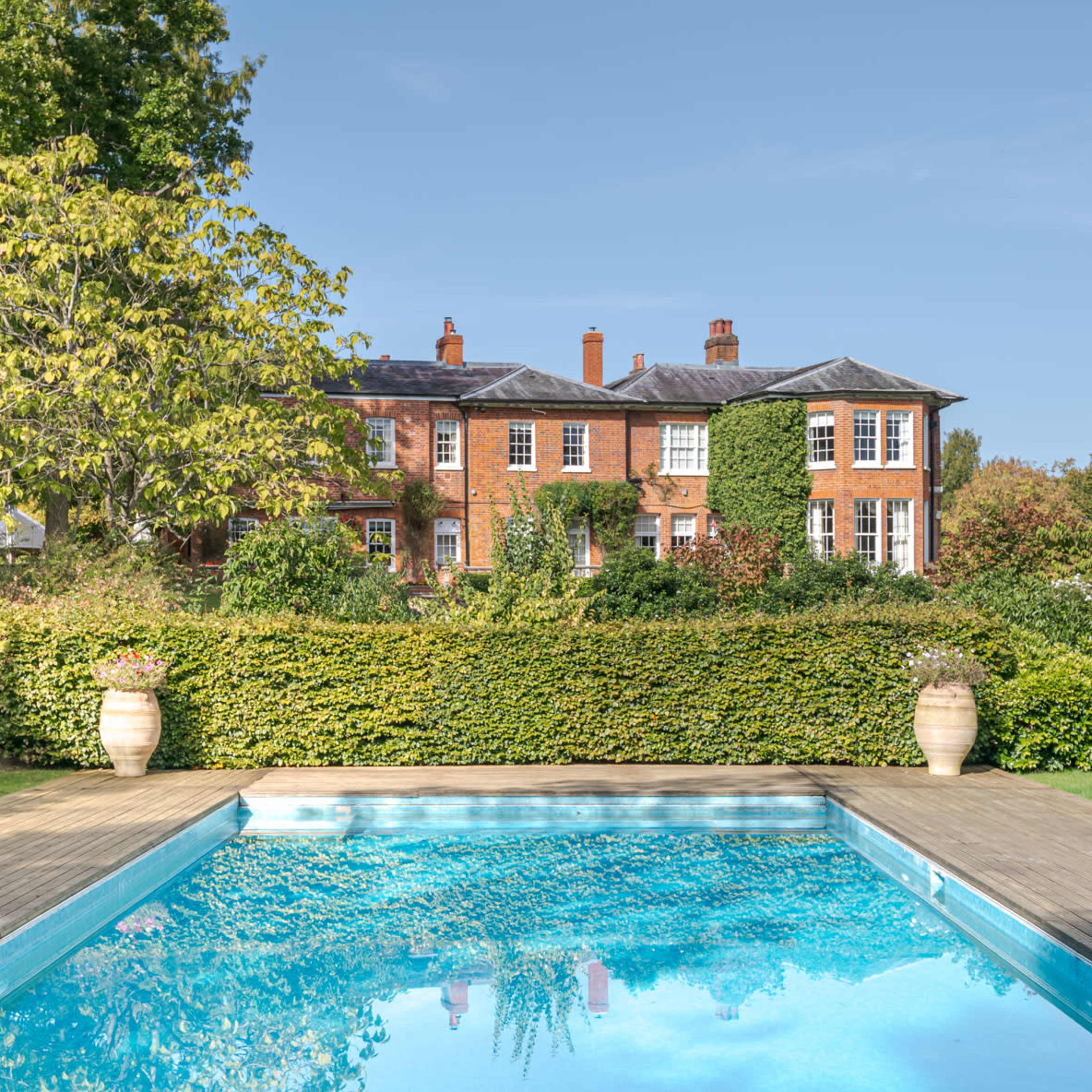 A grand brick house with a large staircase and symmetrical landscaping is set against a clear sky.