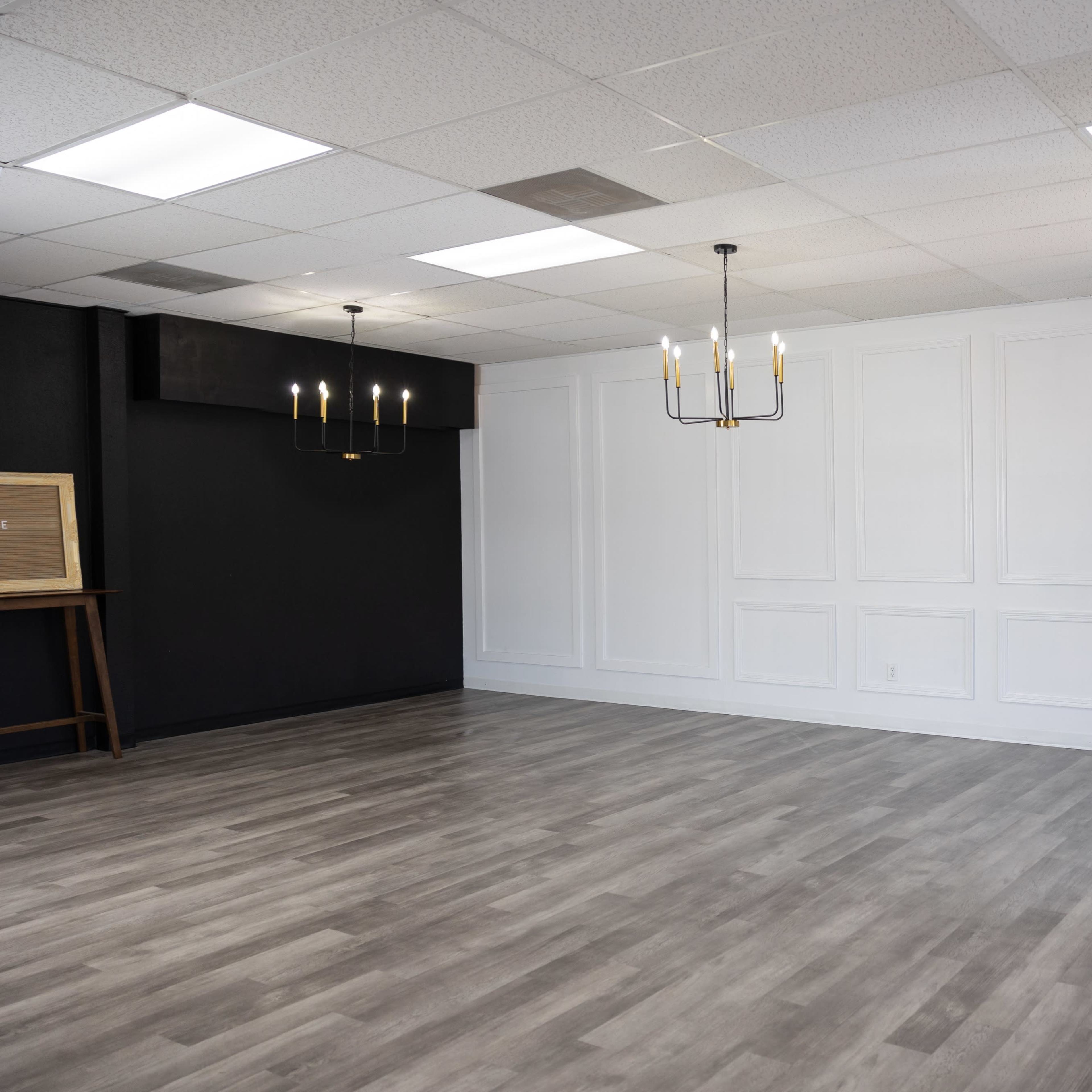 A spacious, empty room with a light-colored floor, white walls with decorative paneling, and three chandeliers hanging from the ceiling.