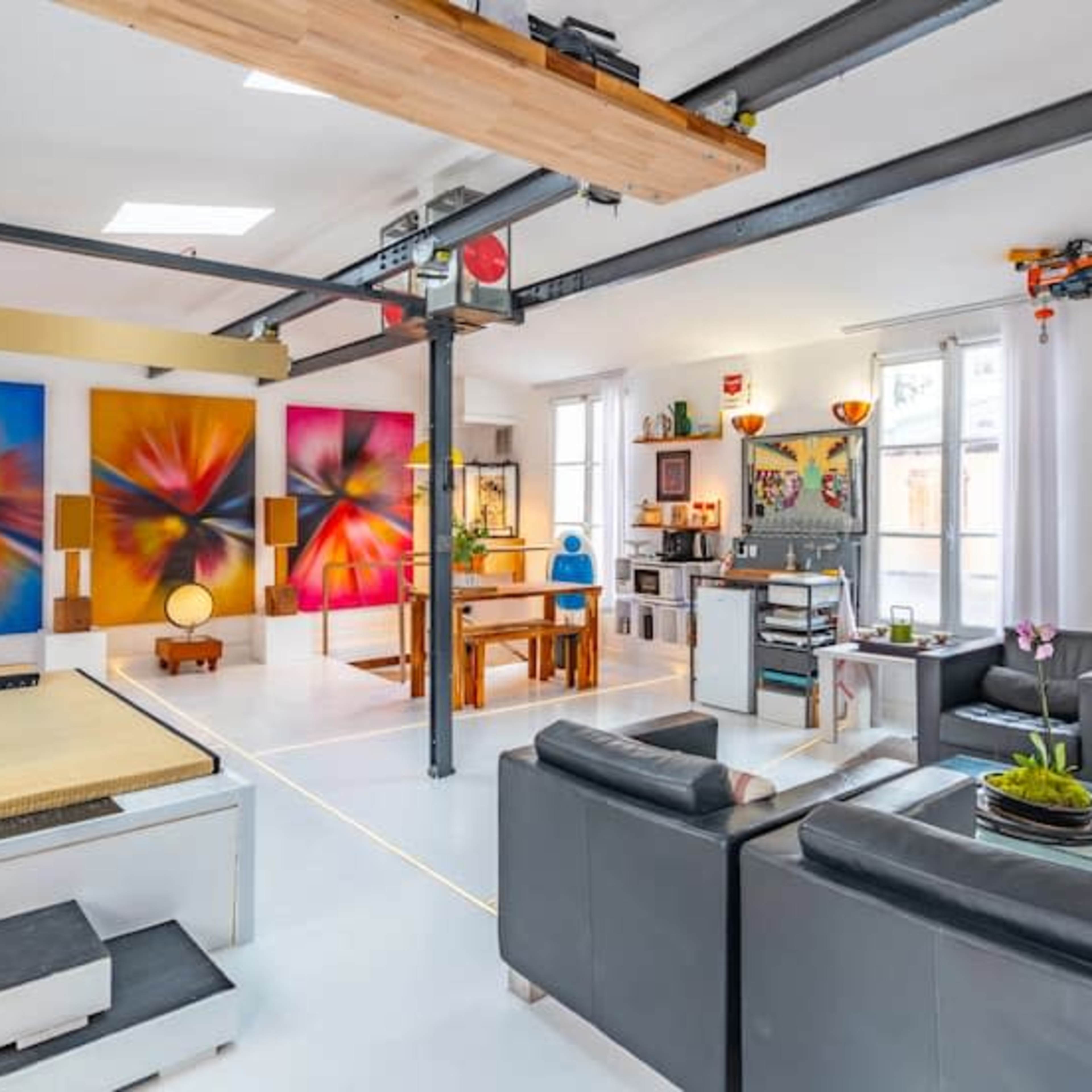 A spacious, modern living area with bright wall art, a dining table, and a seating arrangement featuring black leather sofas.