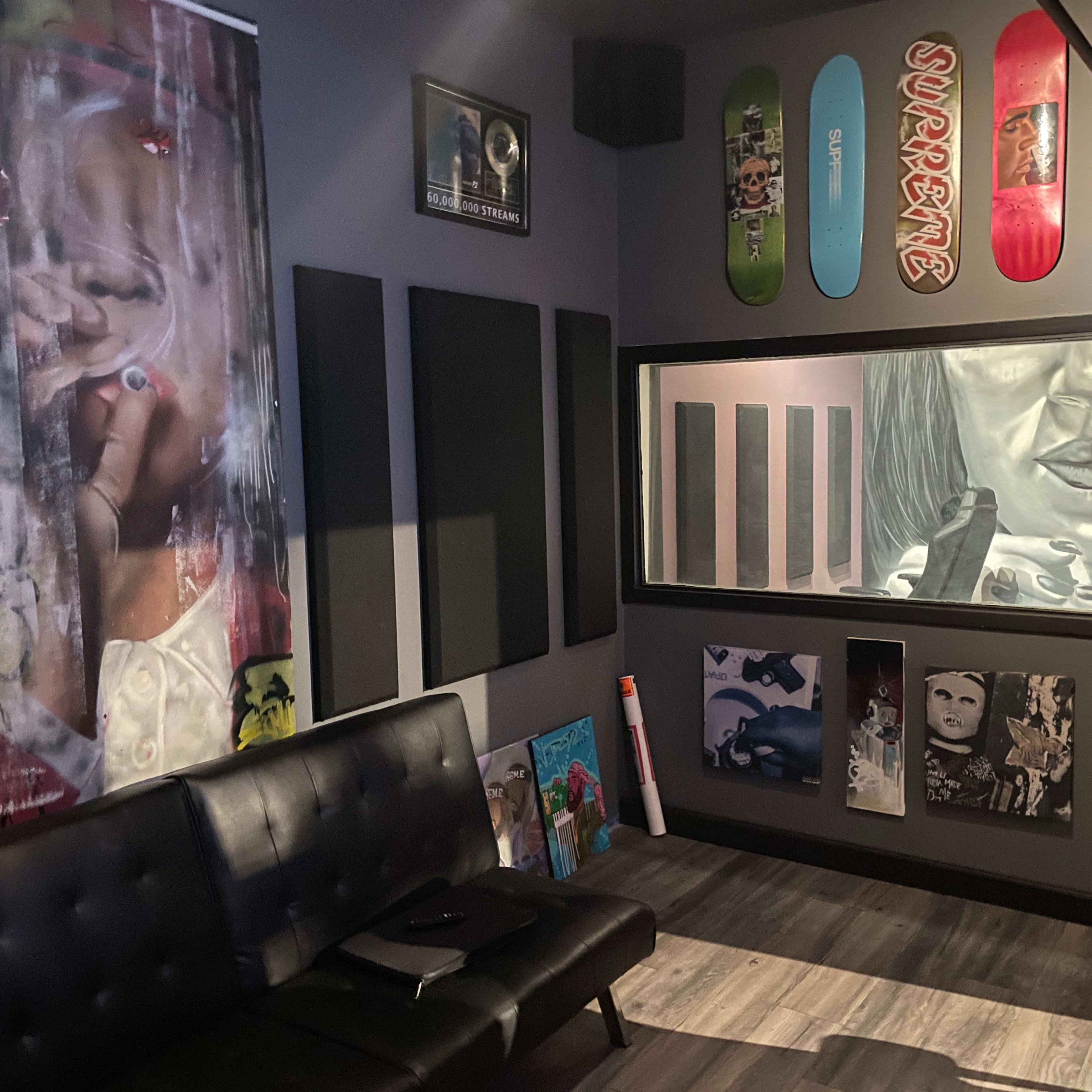 A modern lounge area with a black couch, walls adorned with various artworks, and a window displaying a large monochromatic drawing.