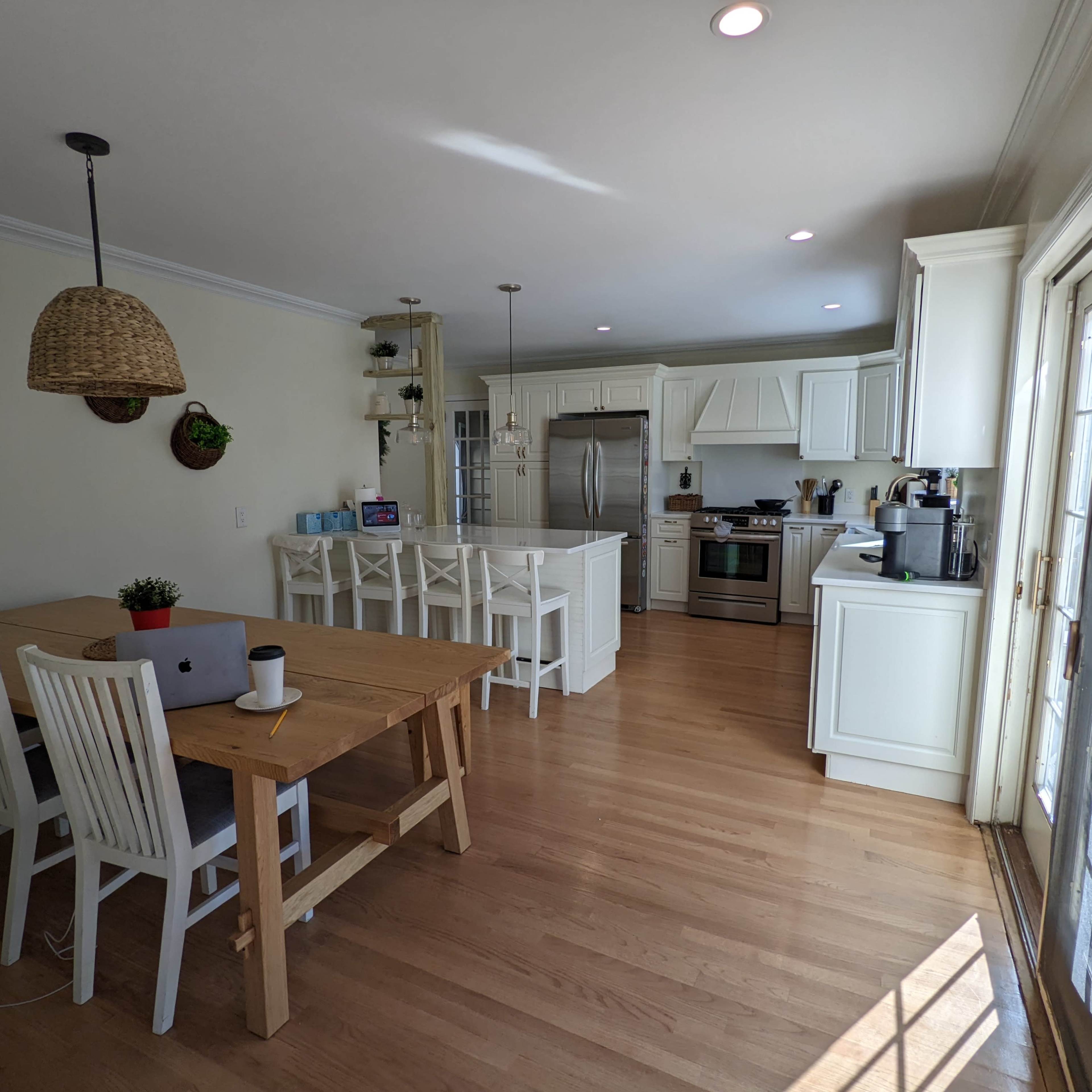 A spacious kitchen and dining area features white cabinetry, a wooden table with chairs, and large windows allowing natural light.